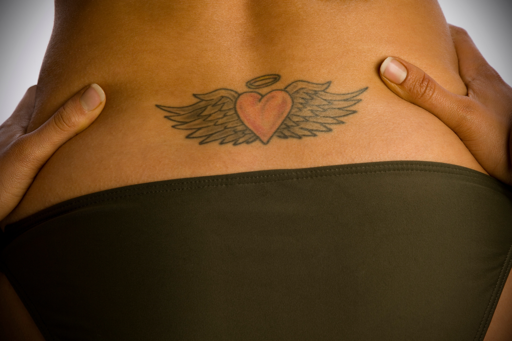 A tattoo of a winged heart with a halo on someone's lower back, partially visible above the waistband of a swimsuit