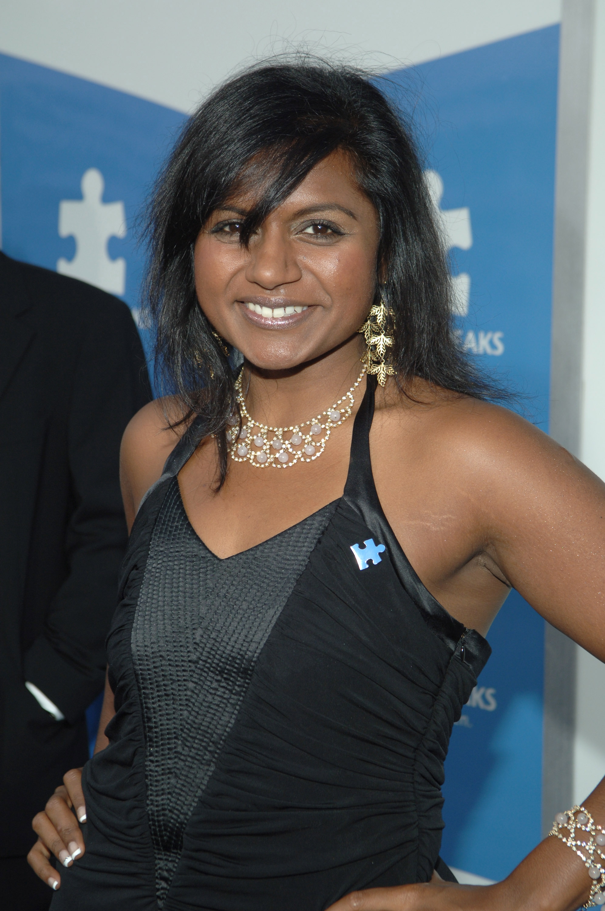 Person in a sleeveless black dress with gold jewelry, smiling at a formal event