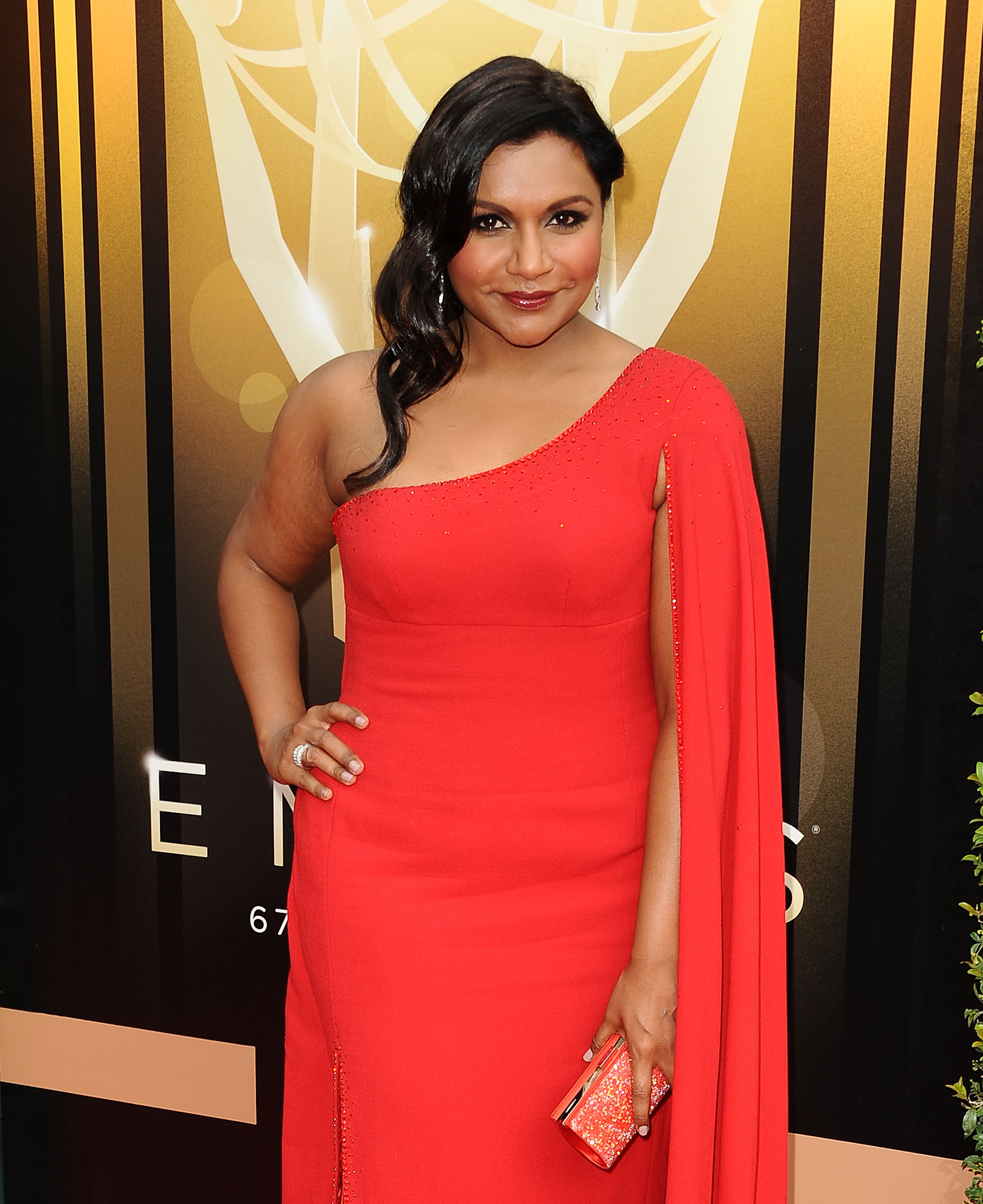 A person on the red carpet in an elegant, one-shoulder dress, holding a matching clutch, posing confidently