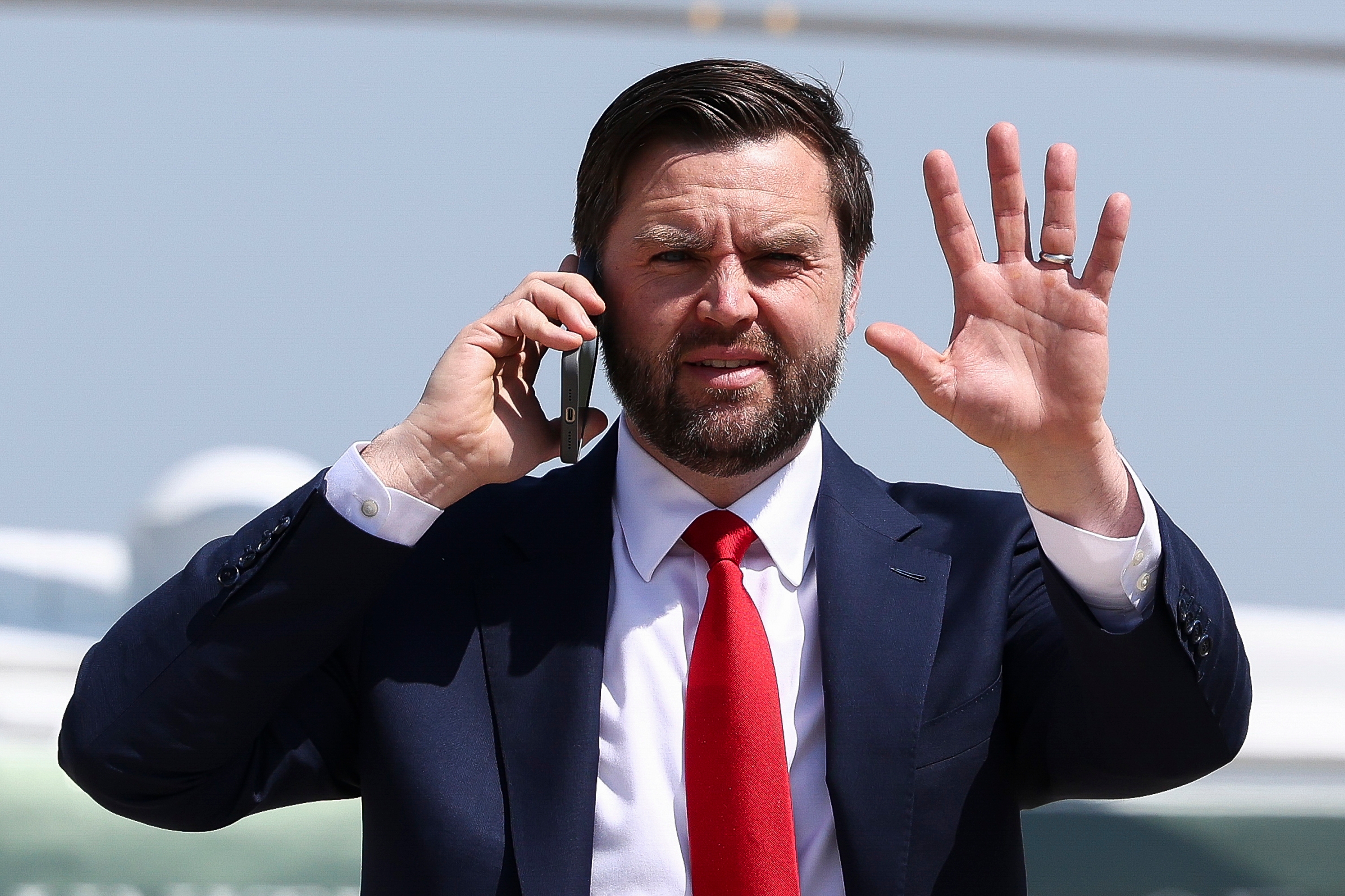 A man in a suit with a red tie is talking on the phone and waving