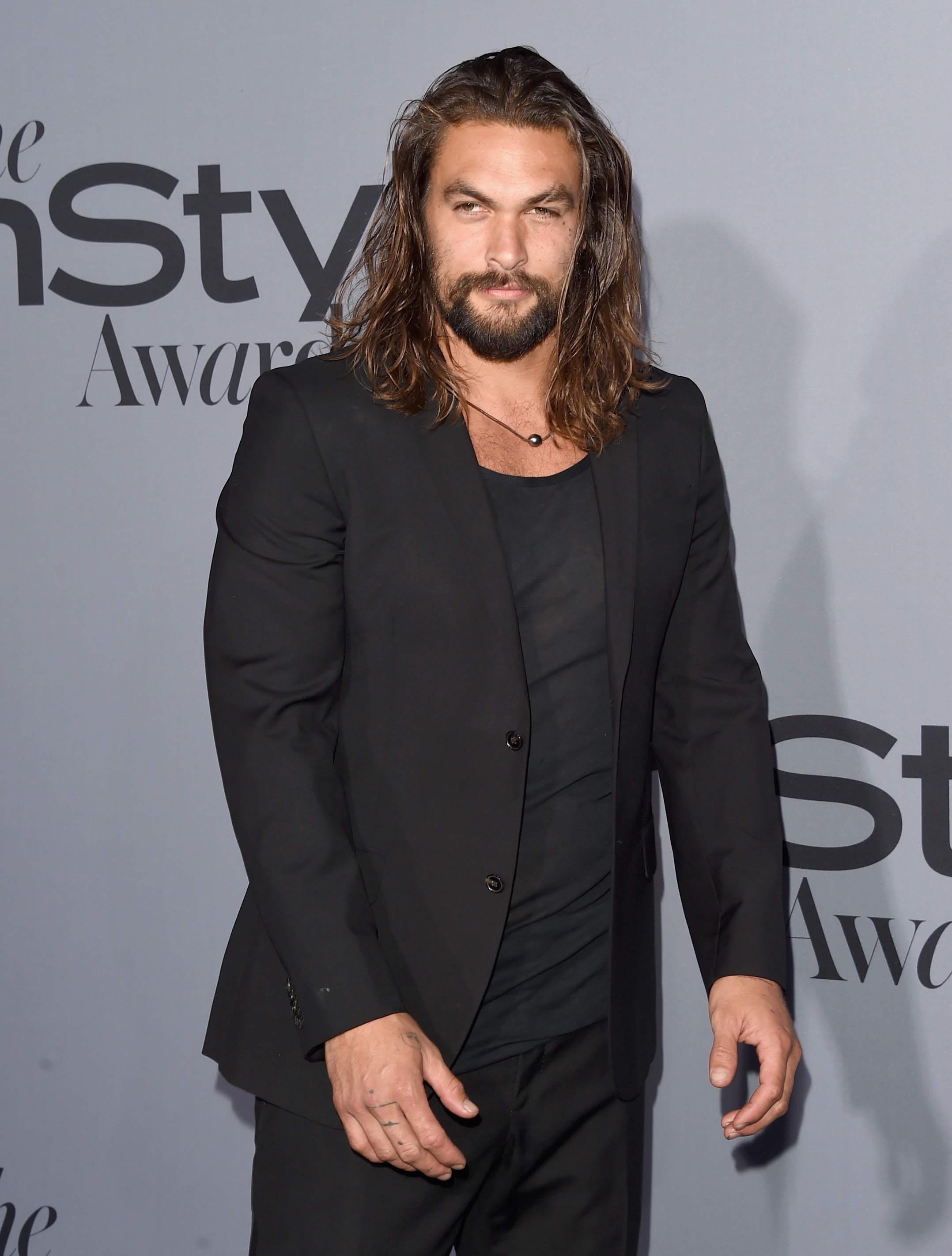 A man with long hair, beard, and mustache wearing a black suit and shirt at a formal event