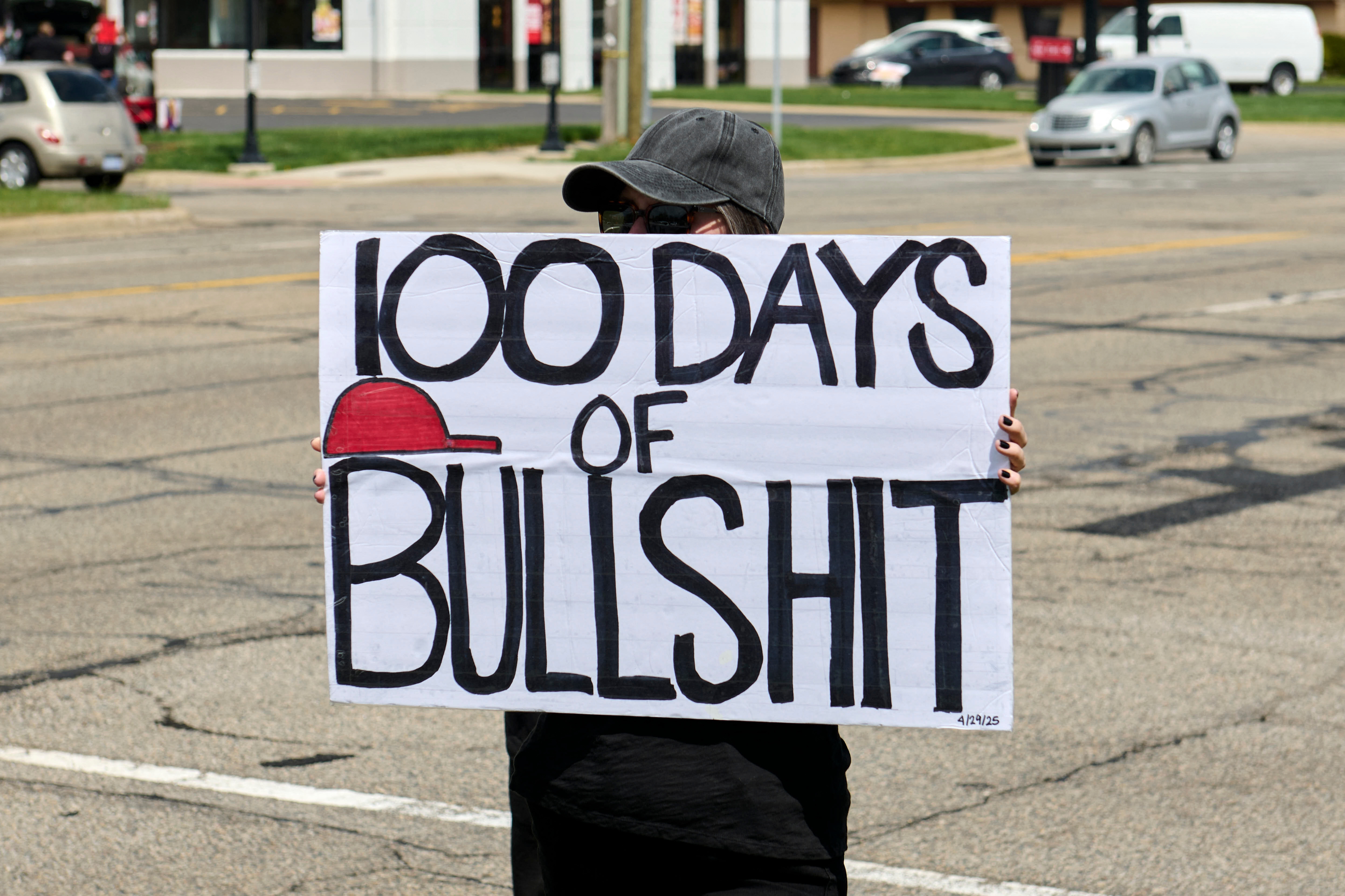 Person holding sign reading "100 days of bullshit" in a street protest setting