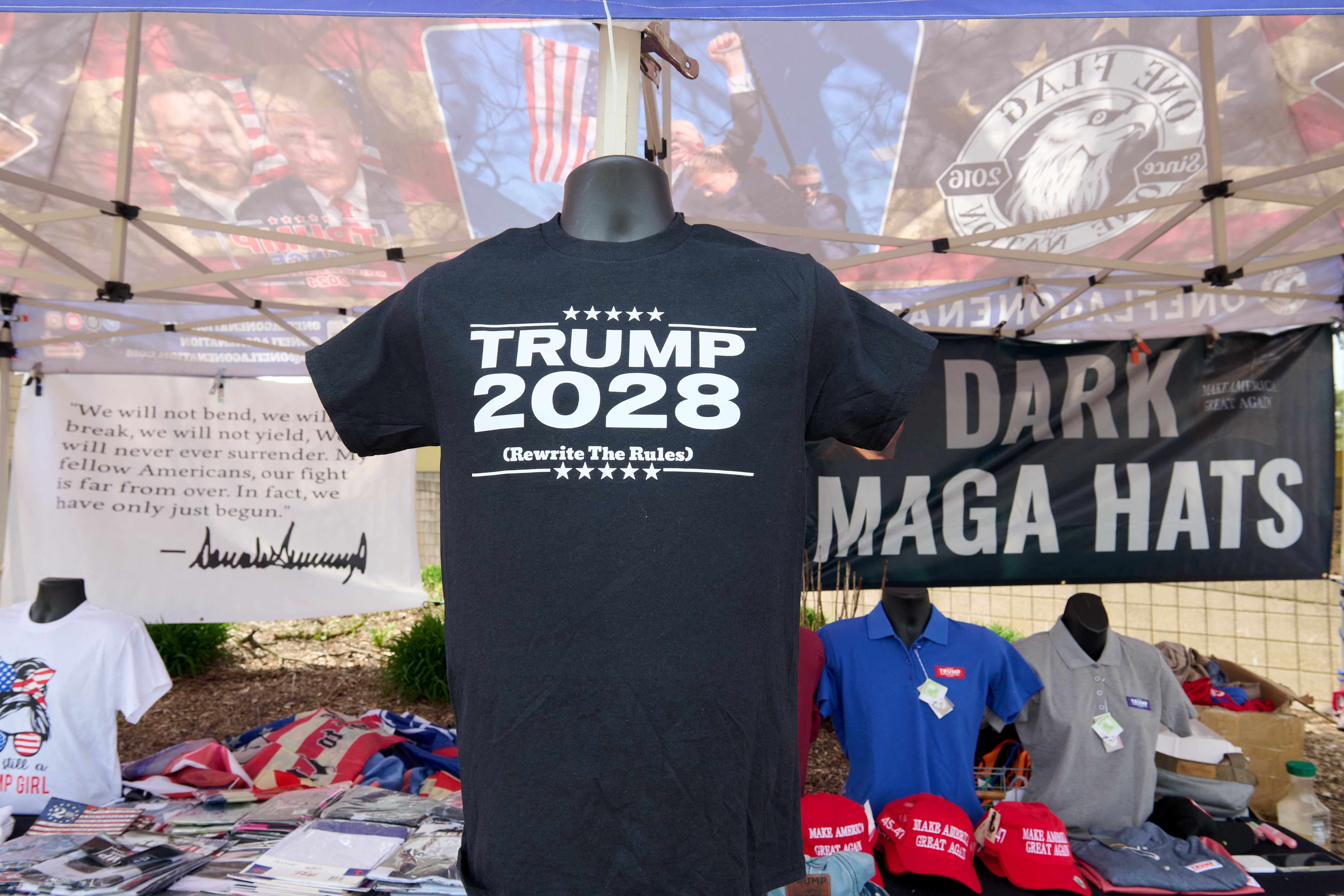 T-shirt display at a booth featuring "Trump 2028" text, surrounded by merchandise including "Dark MAGA Hats" and pro-Trump apparel
