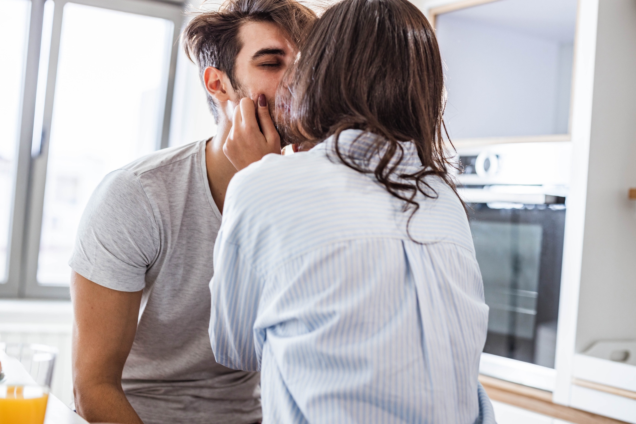 A couple shares a tender moment in a kitchen, facing each other closely