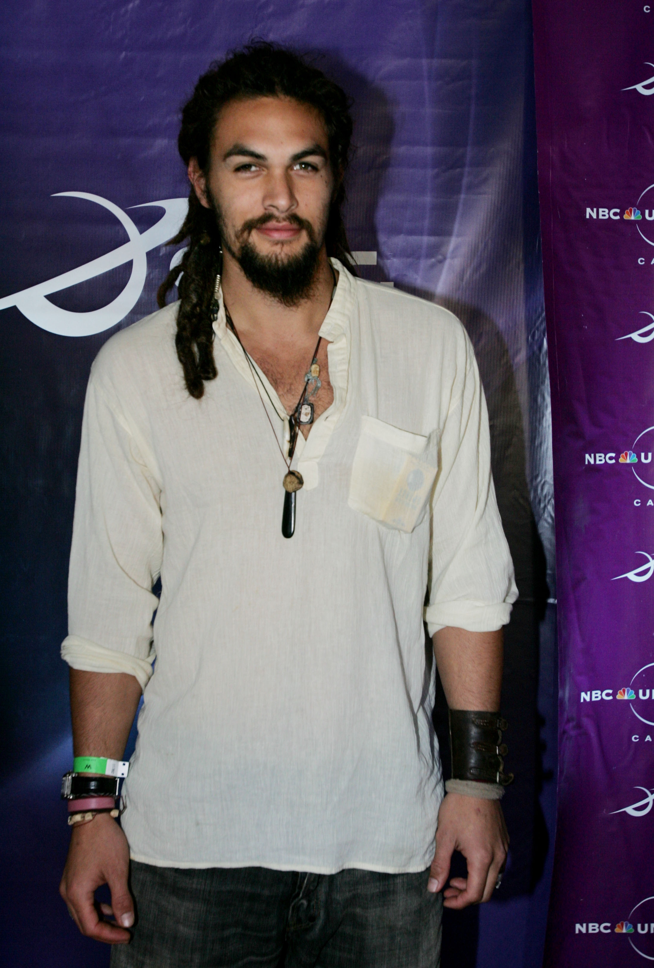 Person with long hair and beard in casual attire, wearing a loose shirt, necklaces, bracelets, and leather wristbands at a celebrity event