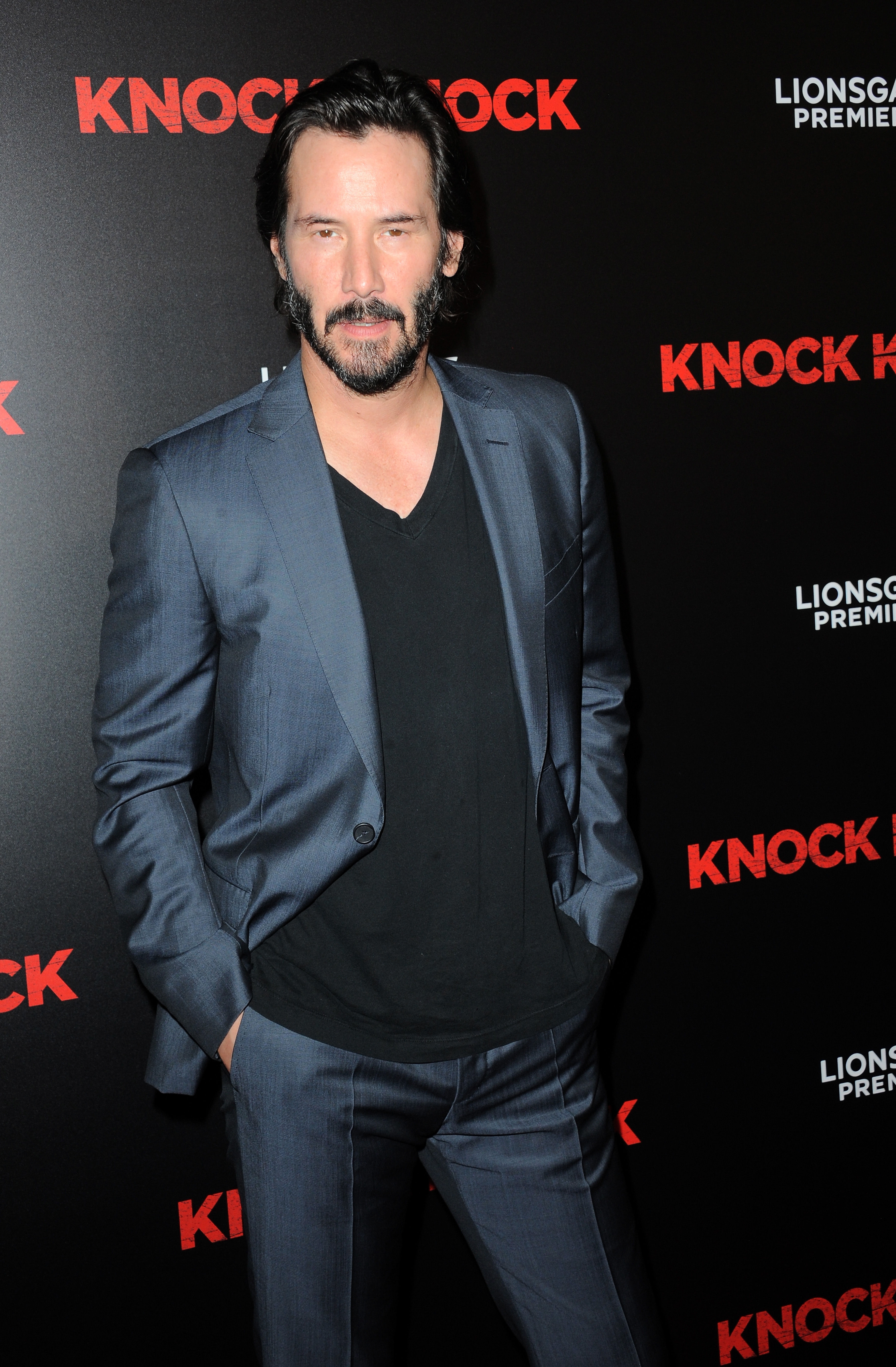Person in a stylish suit at a movie premiere event, standing in front of "Knock Knock" promotional backdrop