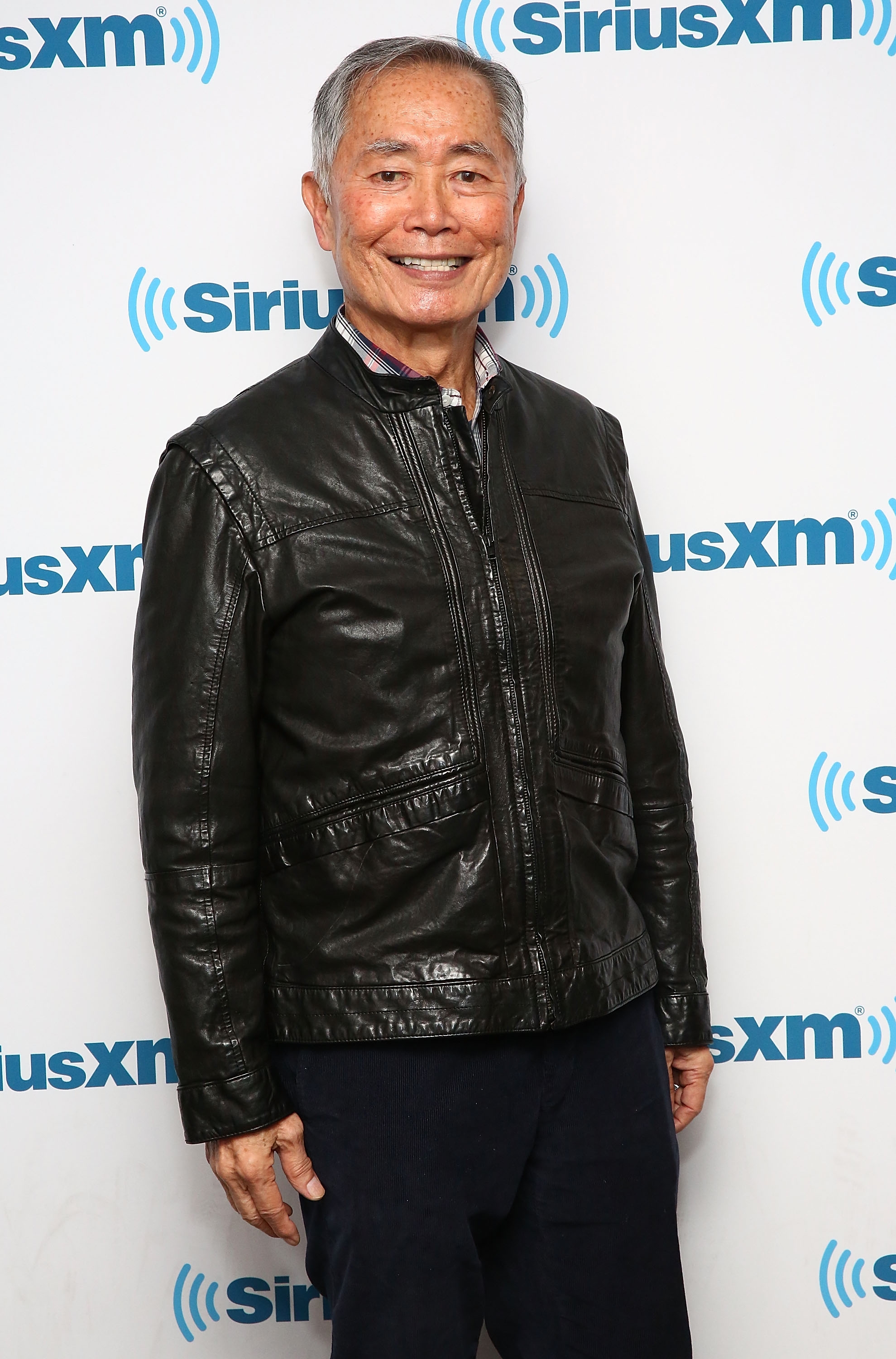 Man in a leather jacket smiles at SiriusXM event backdrop
