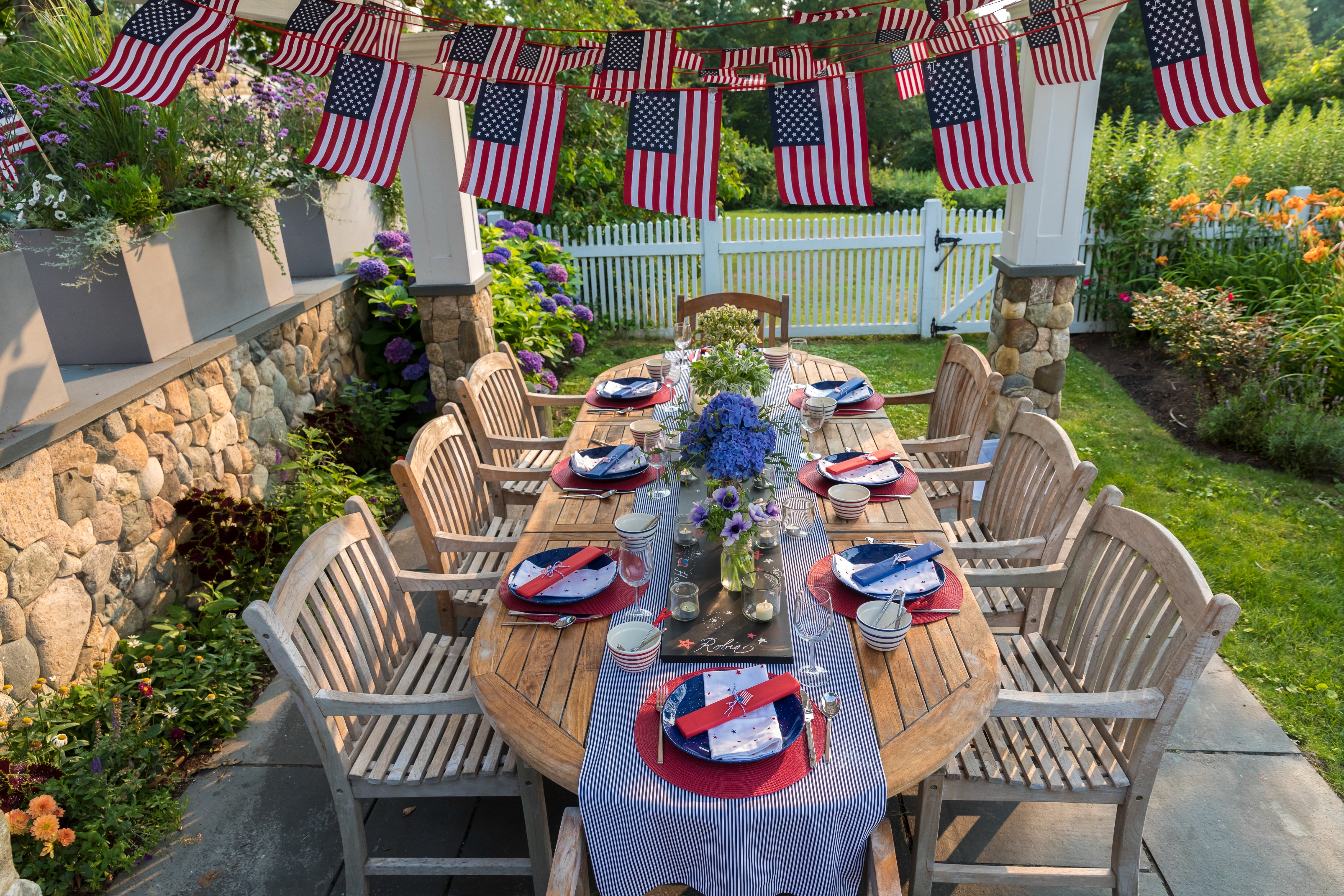 Patriotic outdoor table setting with American flags and floral centerpieces, set for a gathering in a garden