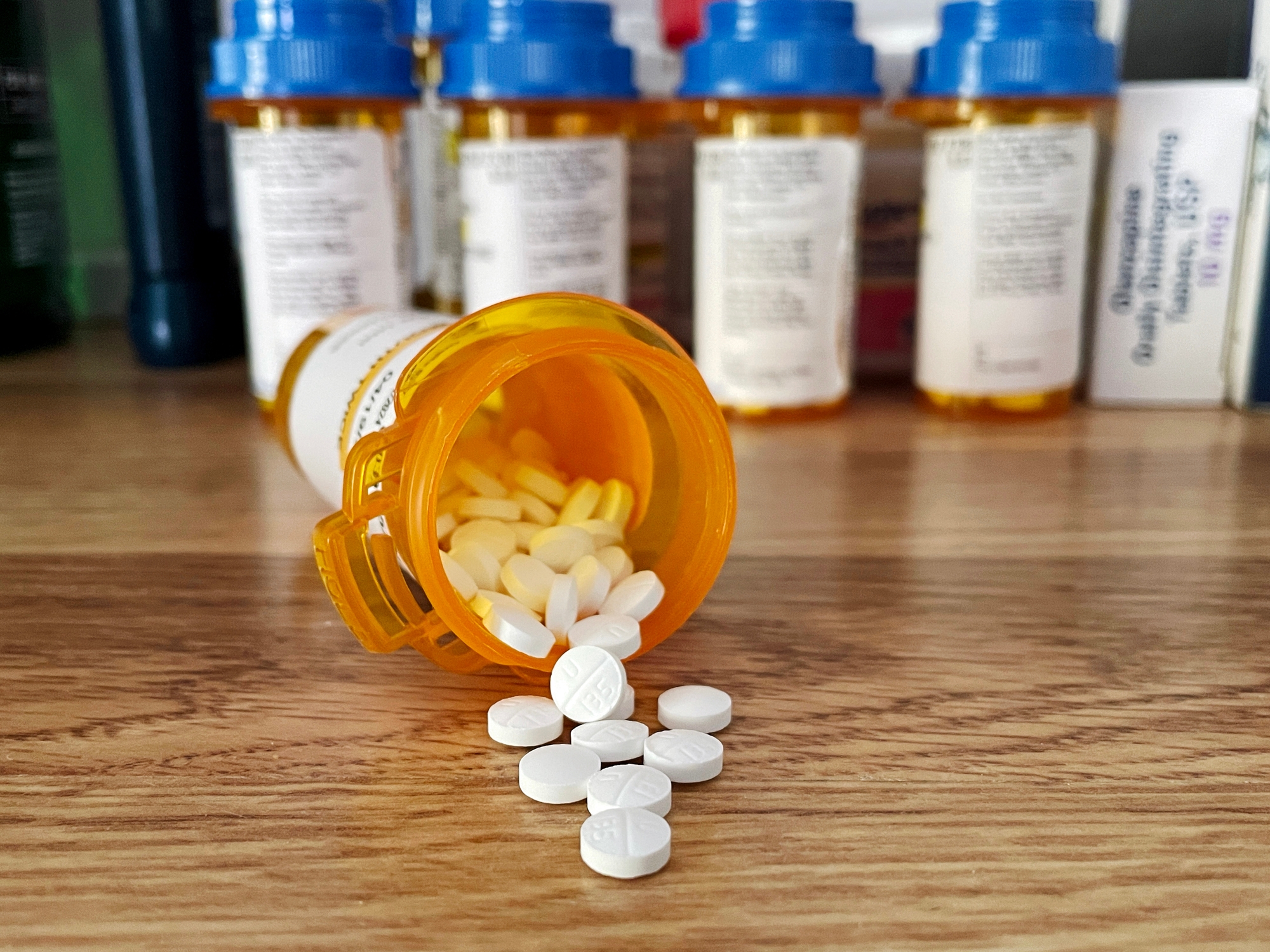 Prescription bottle tipped over with pills spilling out; more medicine bottles in the background