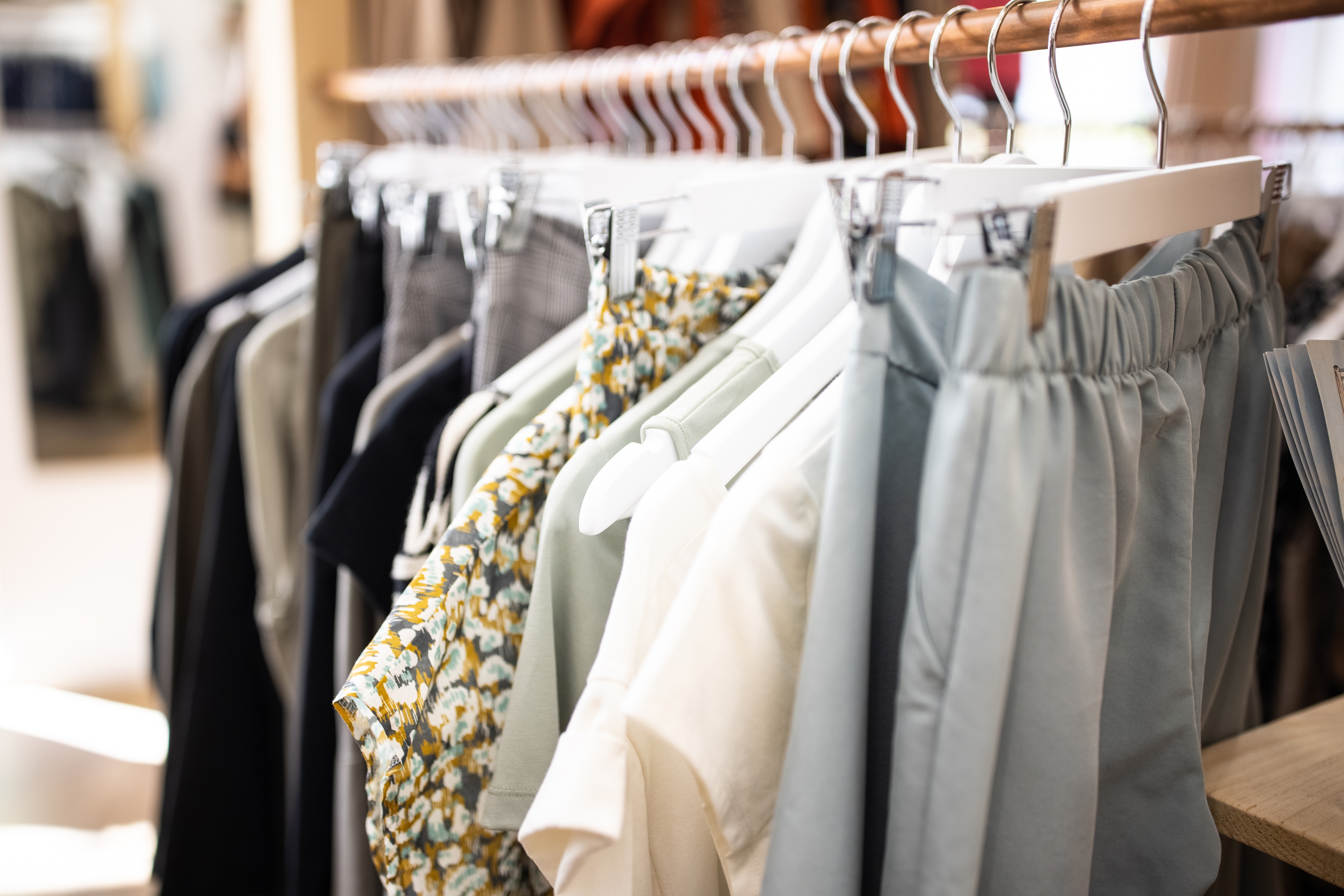 Clothes hanging on a rack, including shirts, pants, and floral dresses, displayed neatly in a store setting