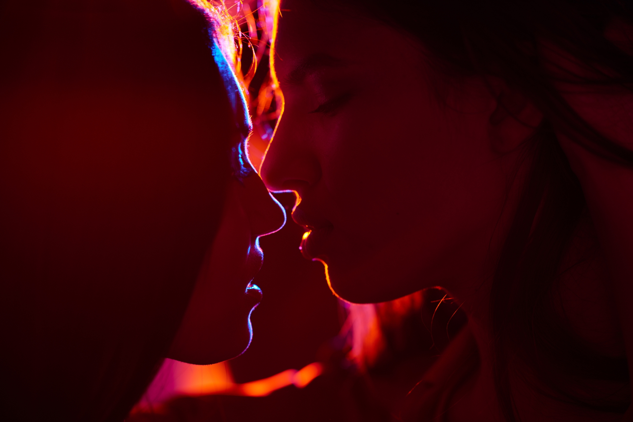 Two people face each other closely in an intimate pose, lit by dramatic lighting