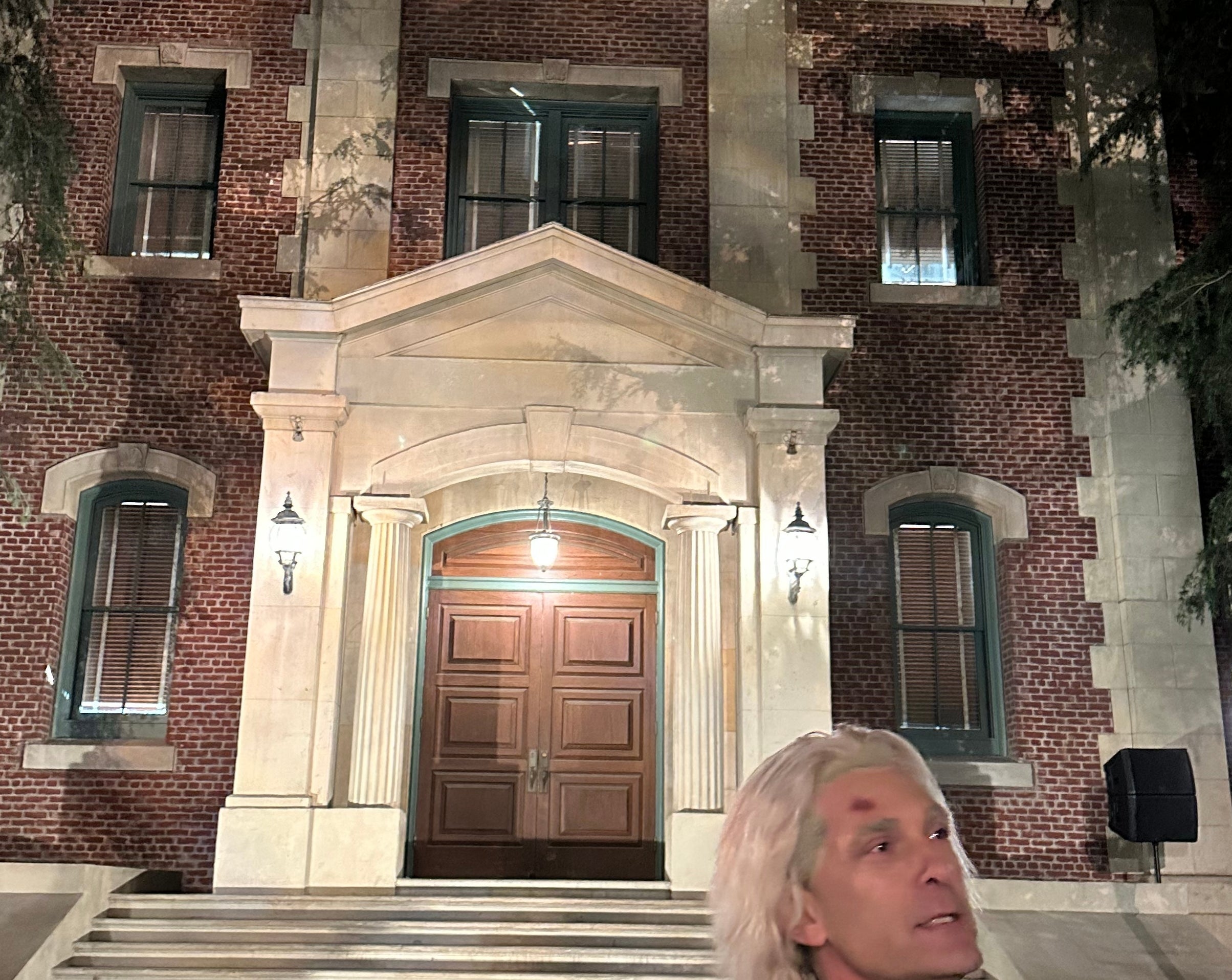 Person stands in front of a historic brick building with a clock above its entrance, holding a book