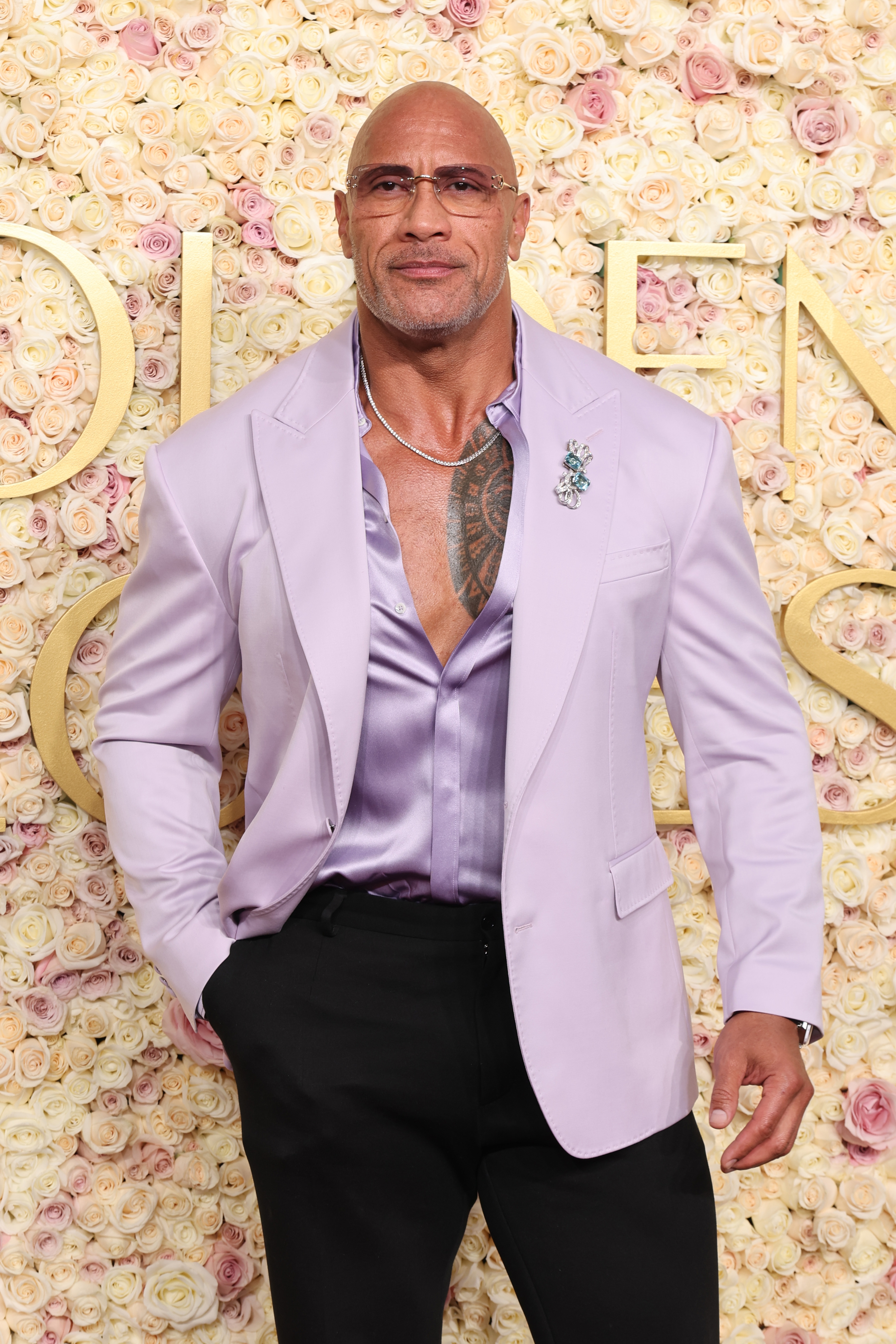 Man in a lavender suit with a satin shirt and floral pin poses on a floral-patterned backdrop