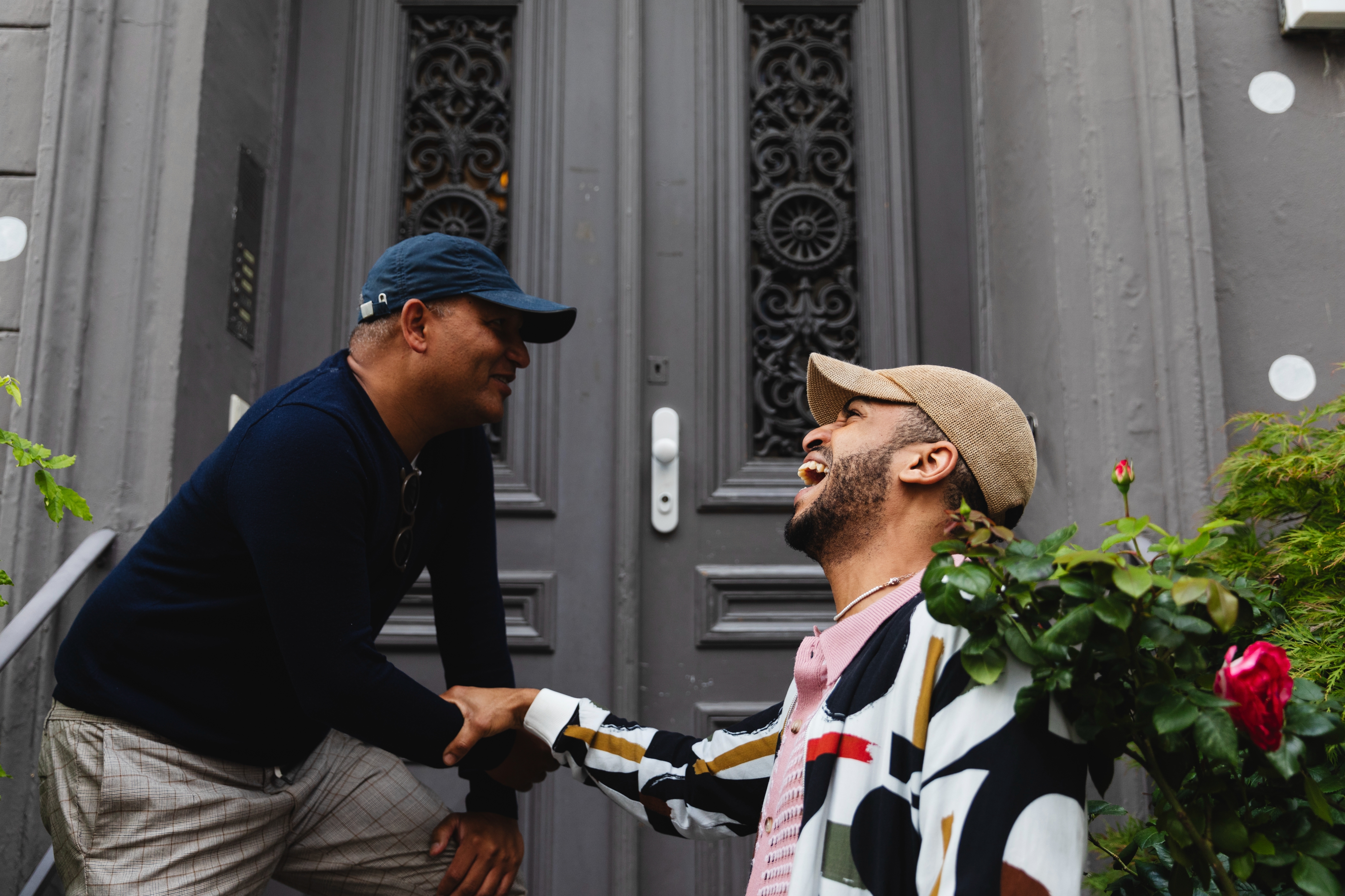 Two people smiling and shaking hands in front of a decorative door, exuding a friendly and amiable vibe