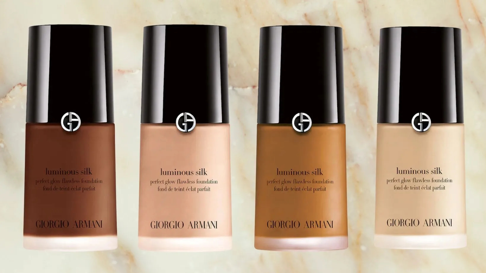 Four bottles of Giorgio Armani Luminous Silk foundation in varied shades displayed against a marble background