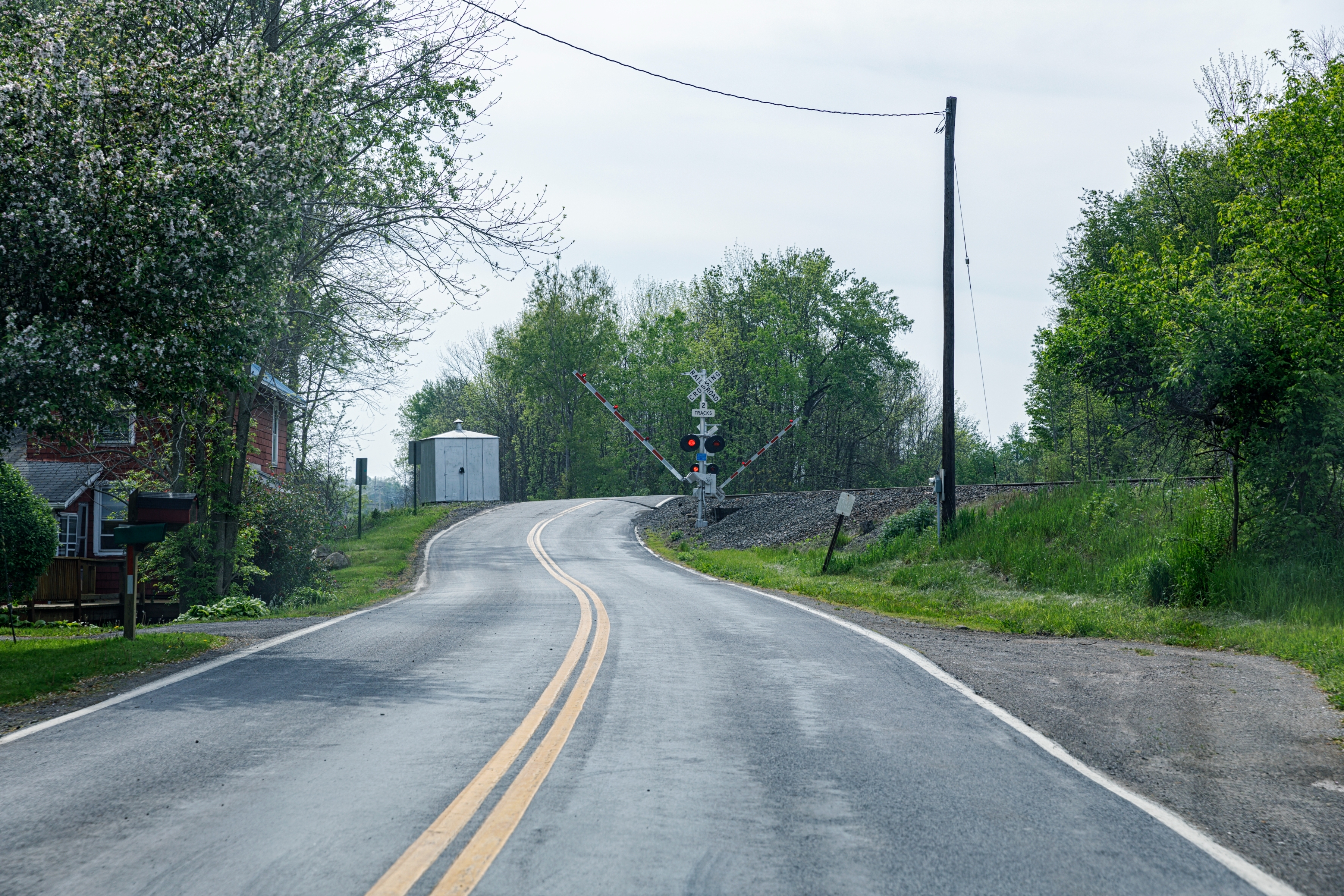 Winding road leading to a railroad crossing with trees on either side and a small building nearby