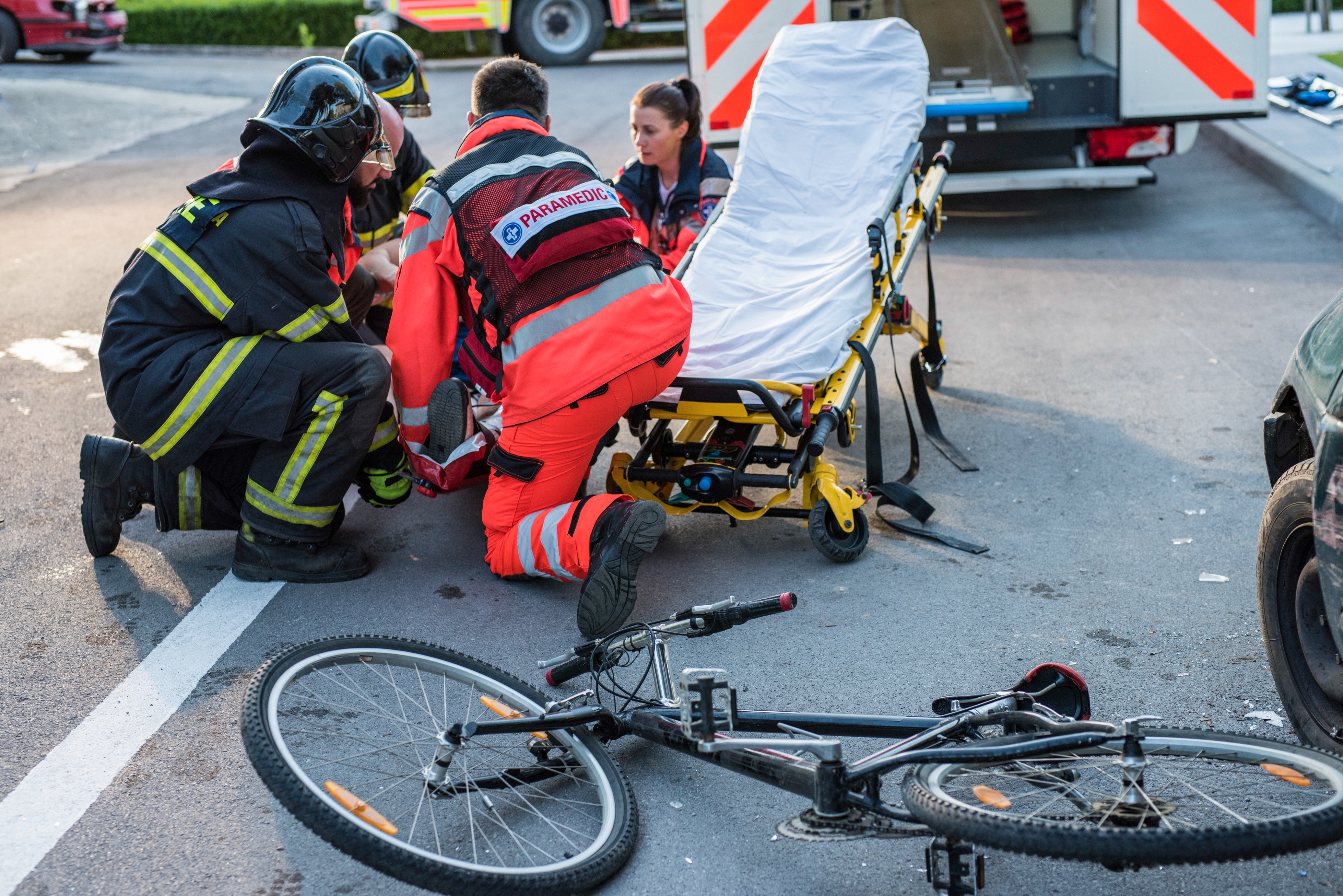 Paramedics assist an injured person on a road beside a bicycle, near an ambulance