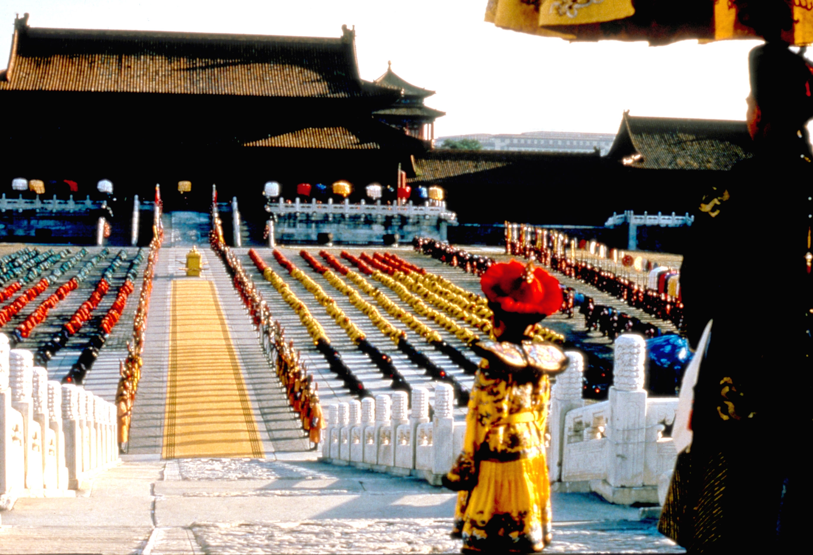 Scene from a historical film set in an ancient palace, featuring ornate architecture and a crowd in traditional attire