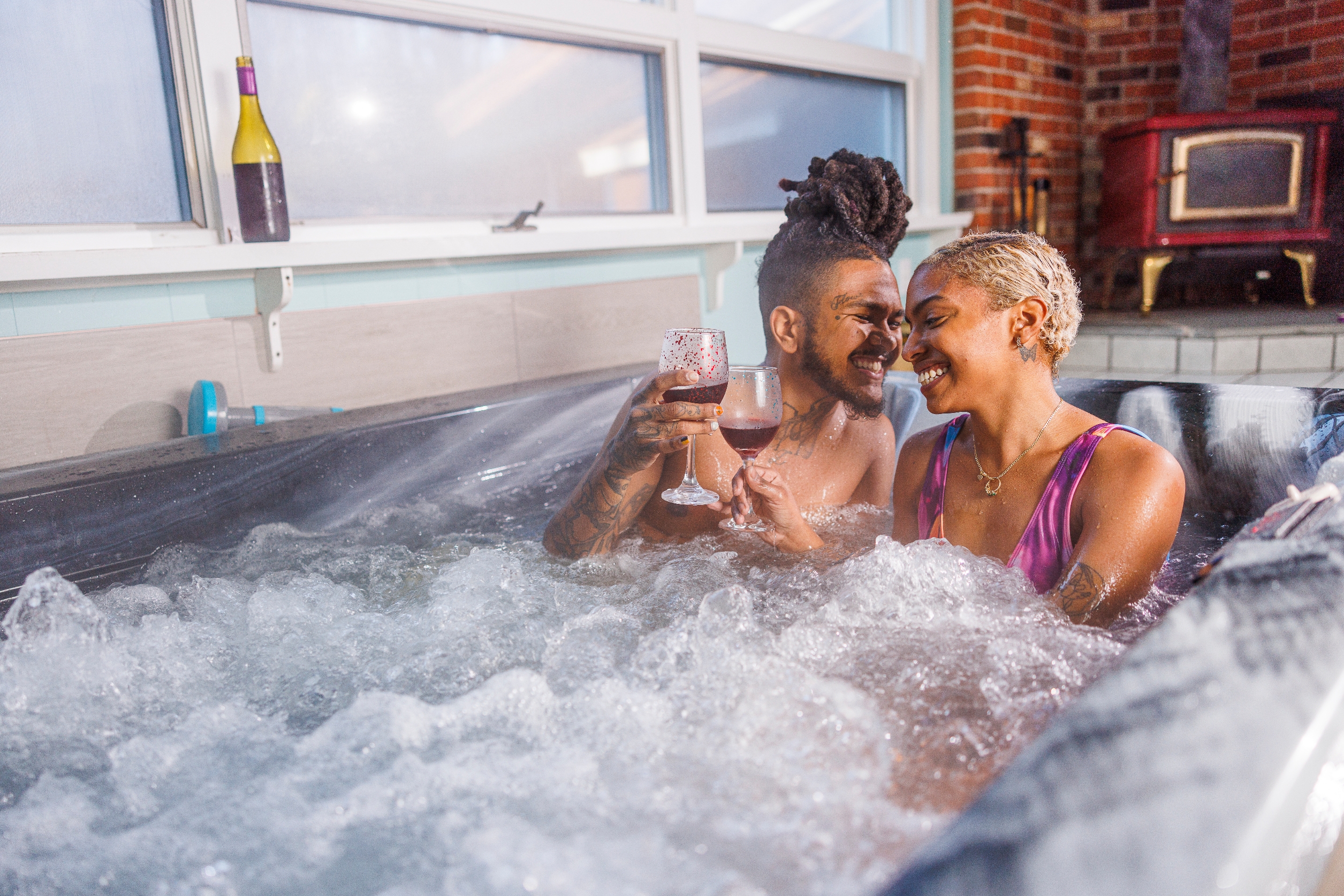 Couple enjoying a romantic moment in a hot tub, toasting with wine glasses, smiling affectionately at each other