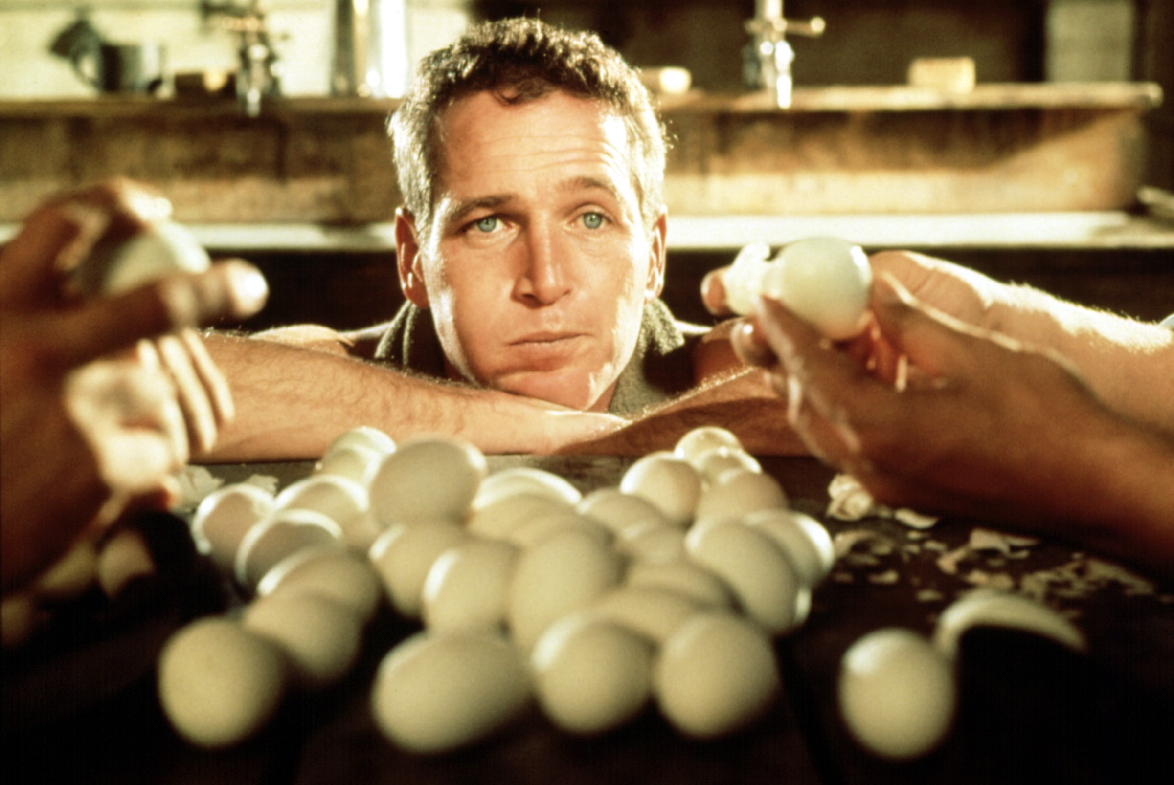 Scene from a classic film with a man observing a large pile of eggs on a table, surrounded by hands holding eggs