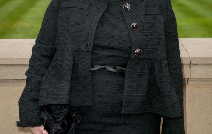 lena in stylish textured outfit stands outdoors by a lawn, posing confidently with elegant accessories