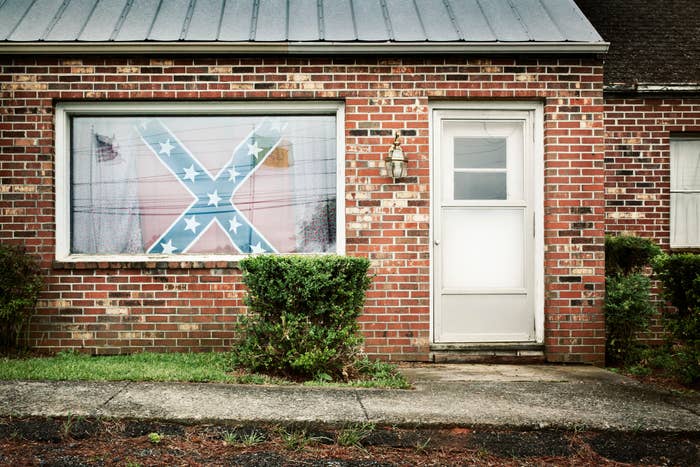 Brick house with a large Confederate flag displayed inside a front window. Bushes line the exterior in front of the house