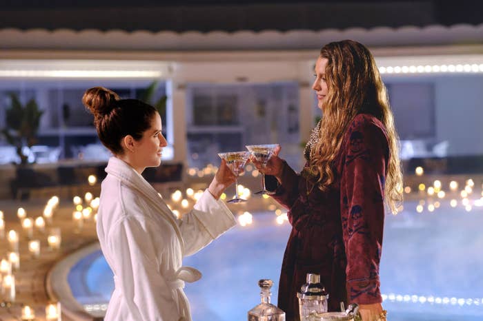 Anna Kendrick and Blake Lively in robes clink glasses at a poolside gathering, surrounded by candles