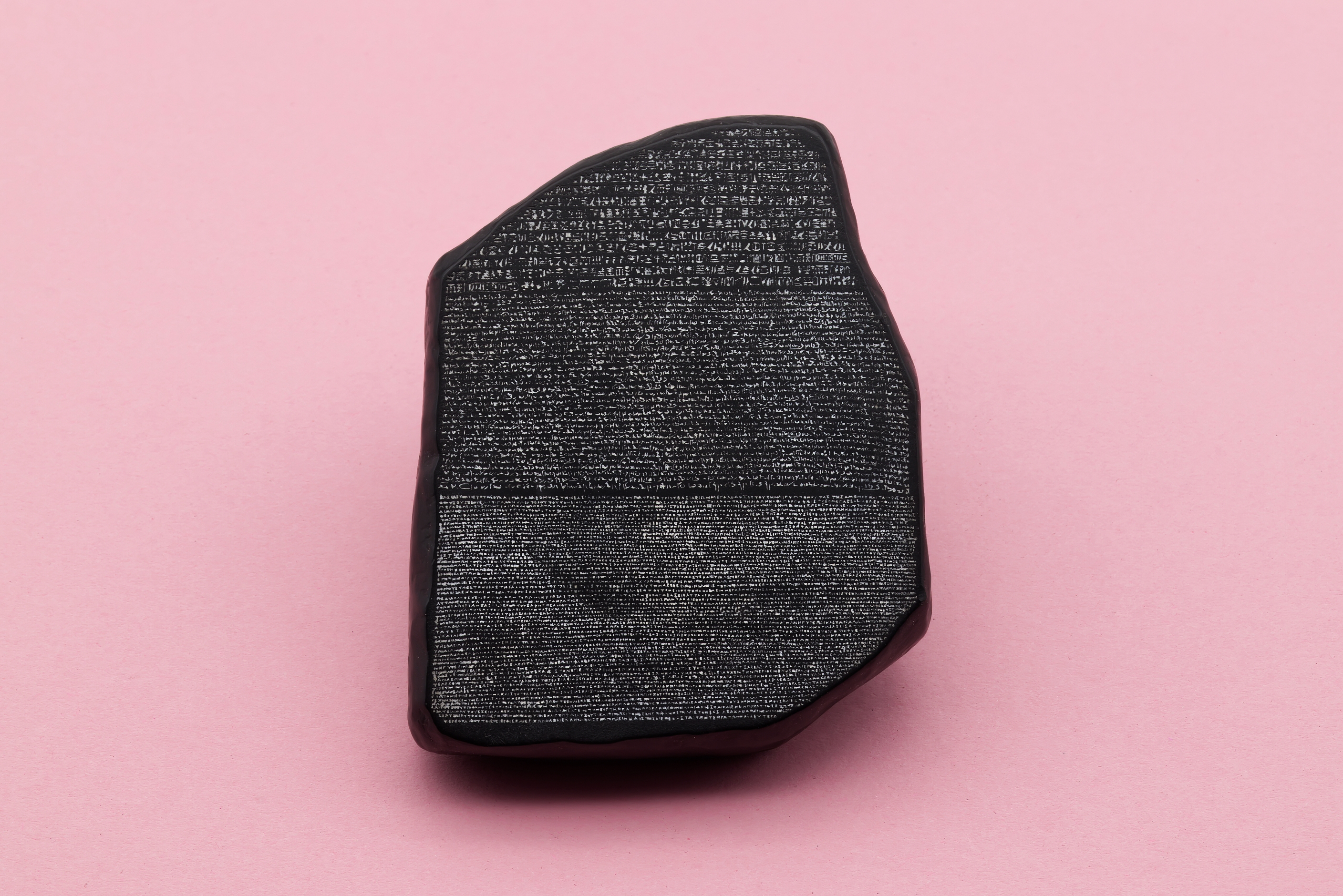 A replica of the Rosetta Stone displayed against a plain pink background