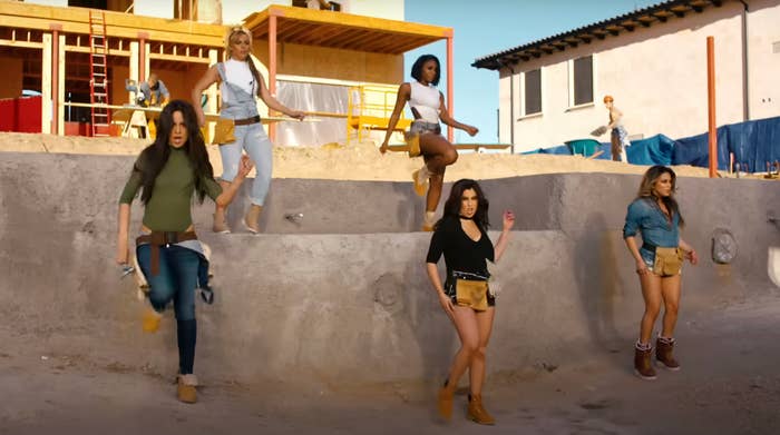 Five women in construction attire pose confidently at a construction site, with a building and tools visible in the background