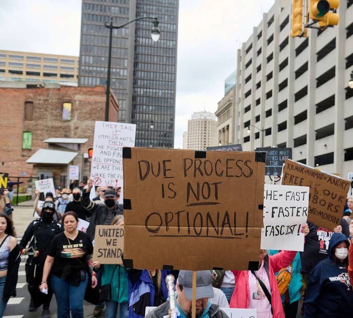 People at a protest hold signs with messages like "Due Process is Not Optional" and "Impeach or Die" in an urban setting