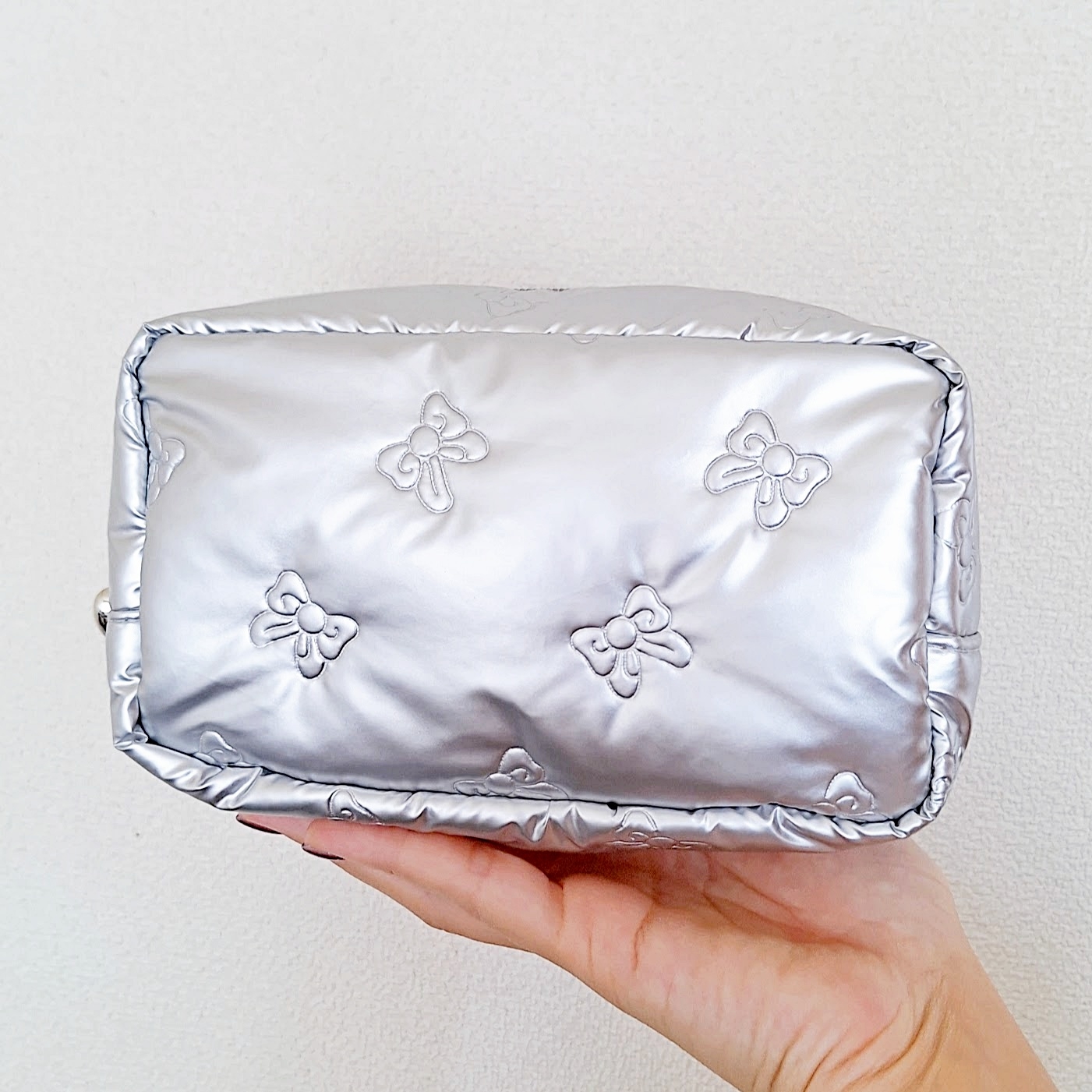 手に持たれた光沢のあるキルティング加工のポーチ。表面に蝶の模様があしらわれている。