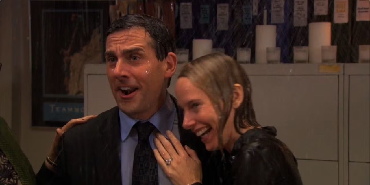 Scene from a TV show where two people, drenched and smiling, stand closely together indoors, creating a joyful and comedic atmosphere