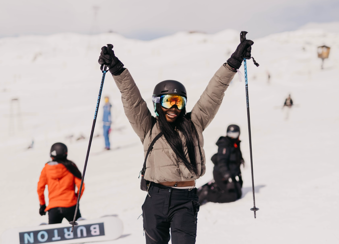 A person in ski gear joyfully raises ski poles on a snowy slope, surrounded by other skiers