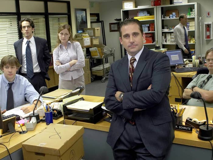 Office staff pose with a confident leader in a suit, showing a busy workplace environment with desks and paperwork