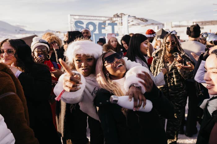 People enjoying an outdoor winter festival, wearing stylish winter clothing and sunglasses, with snow visible on the ground