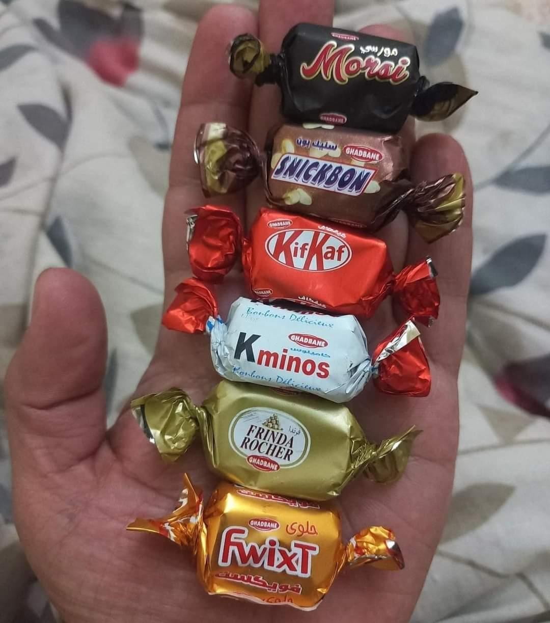 A hand holding six assorted wrapped candies, including brands similar to Snickers, Kit Kat, and Ferrero Rocher