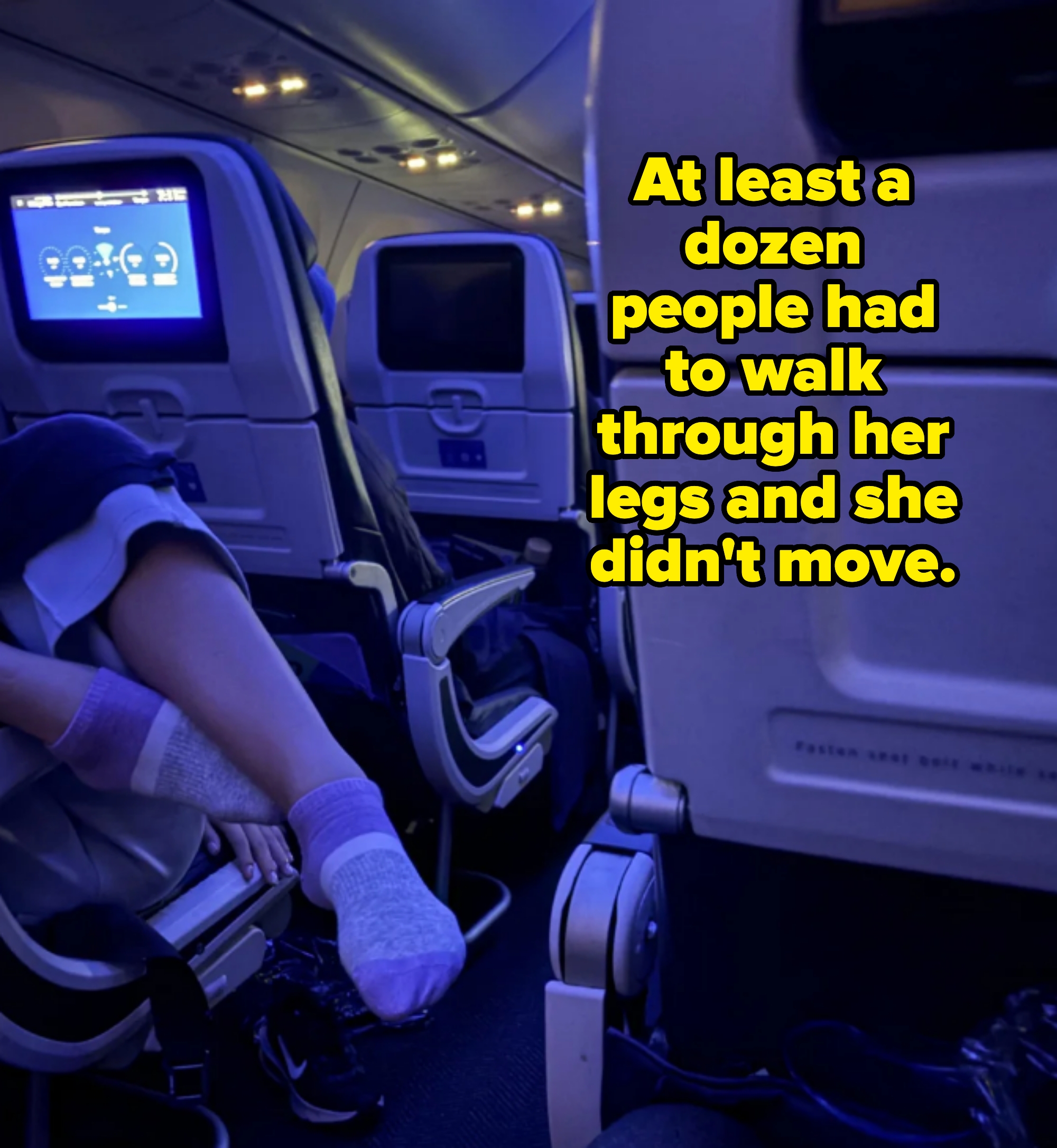 A person on an airplane aisle seat wearing socks rests their feet in the aisle of the plane. Caption: &quot;At least a dozen people had to walk through her legs and she didn&#x27;t move&quot;