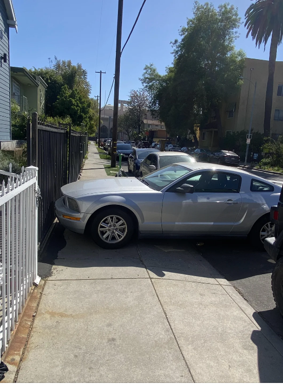 A silver car is parked across a sidewalk, blocking the pathway
