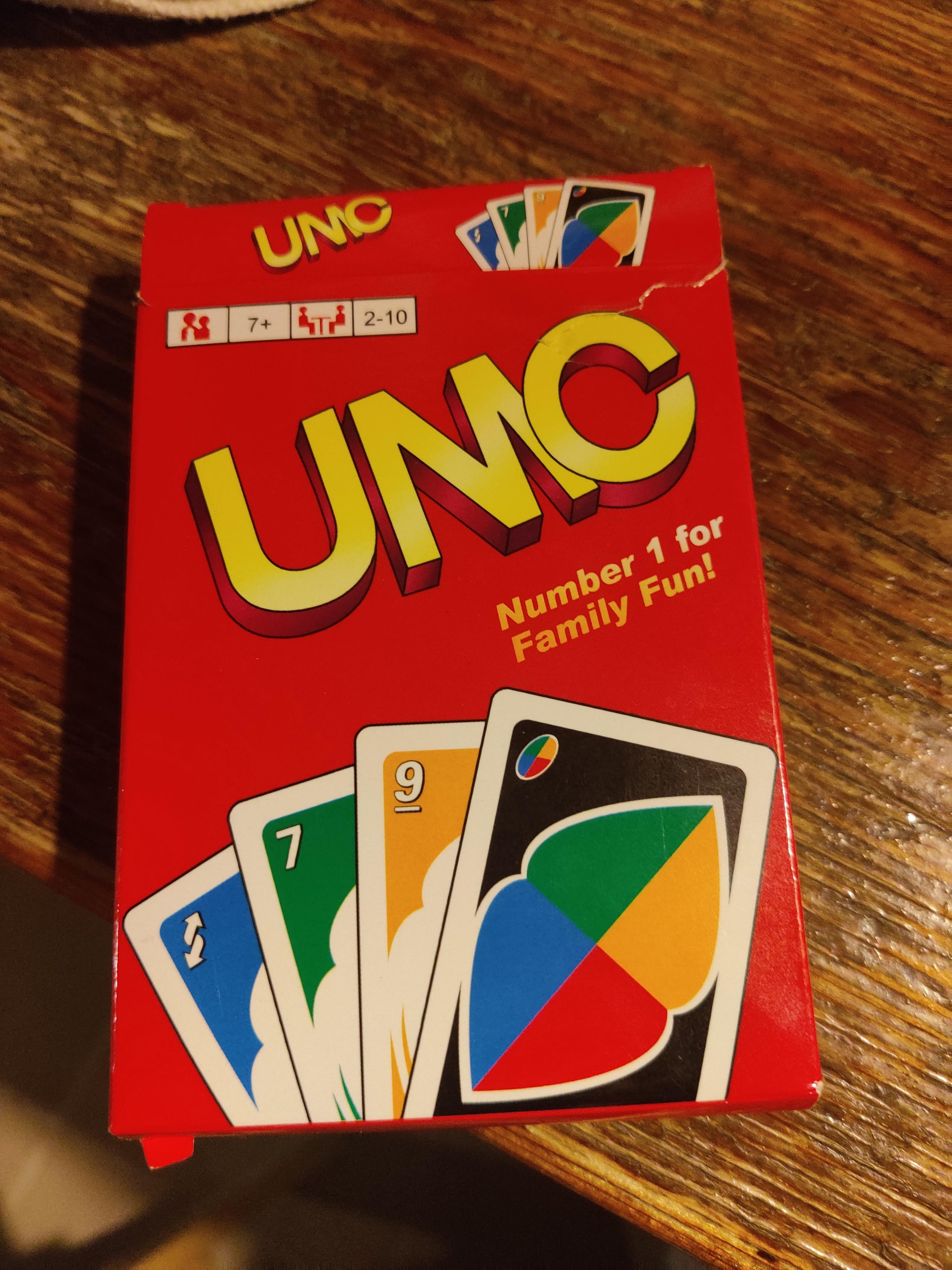 Uno card game box on a table, showing the front with colorful card illustrations and text "Number 1 for Family Fun!"