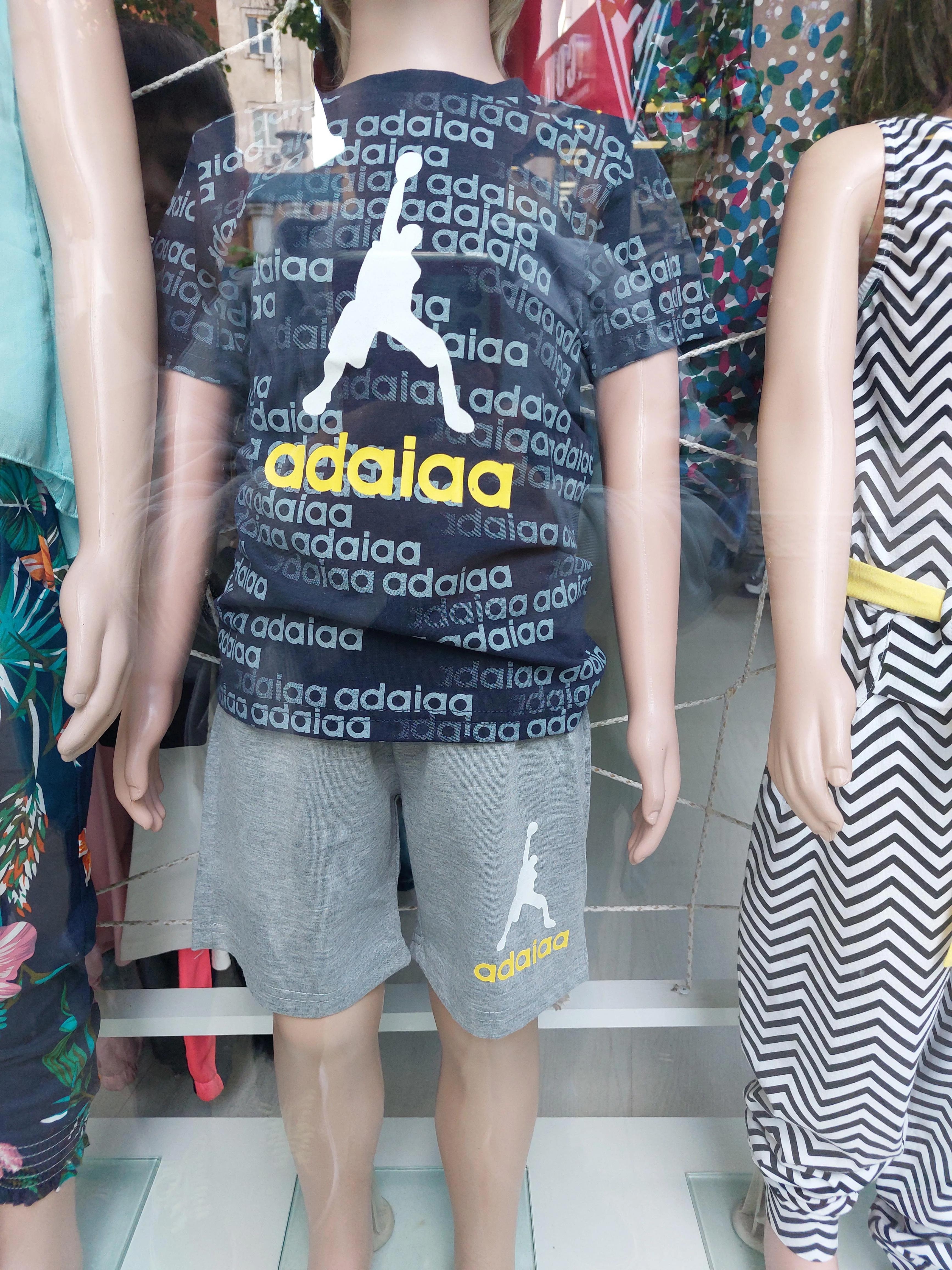Store mannequin wearing a patterned T-shirt and shorts, featuring repeated text and a dancing figure graphic
