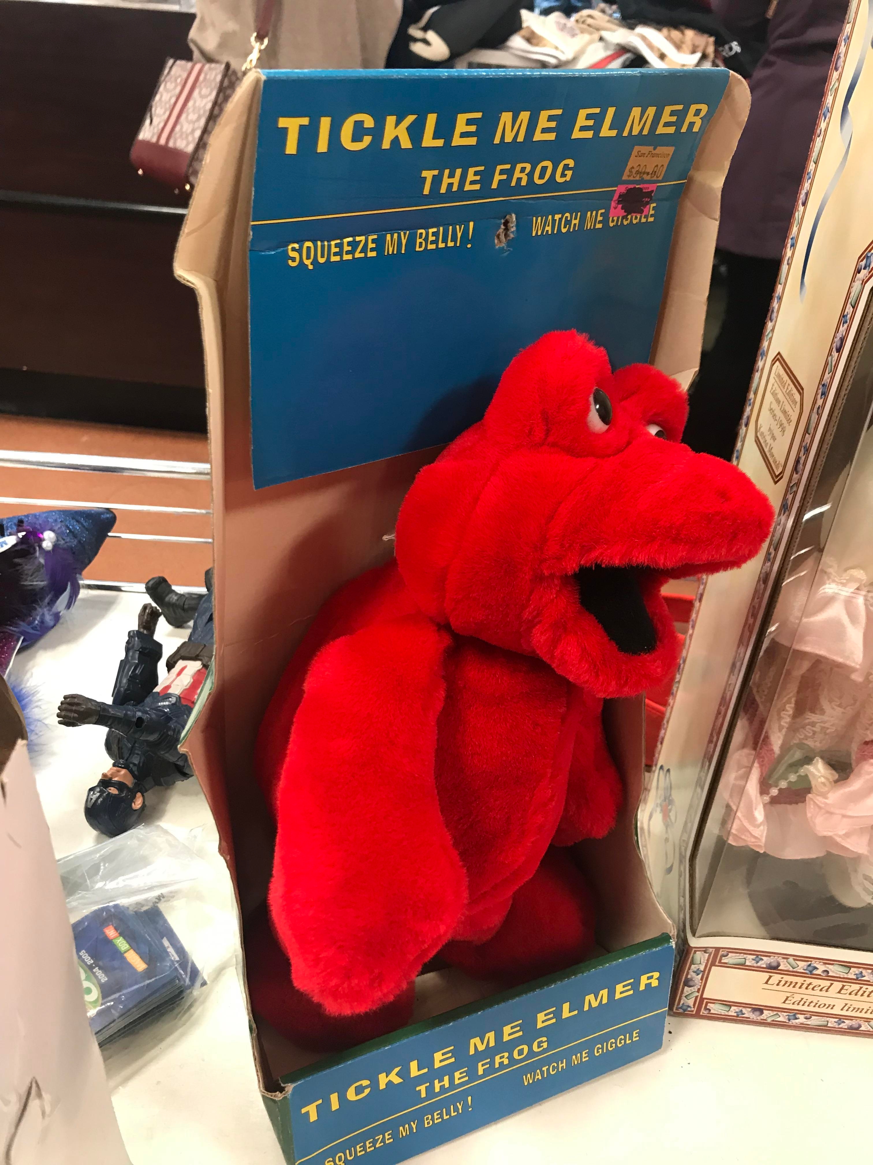 Tickle Me Elmer the Frog toy in packaging, resembling a red Muppet character, displayed on a table