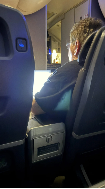 A person seated in an airplane is using a bright laptop
