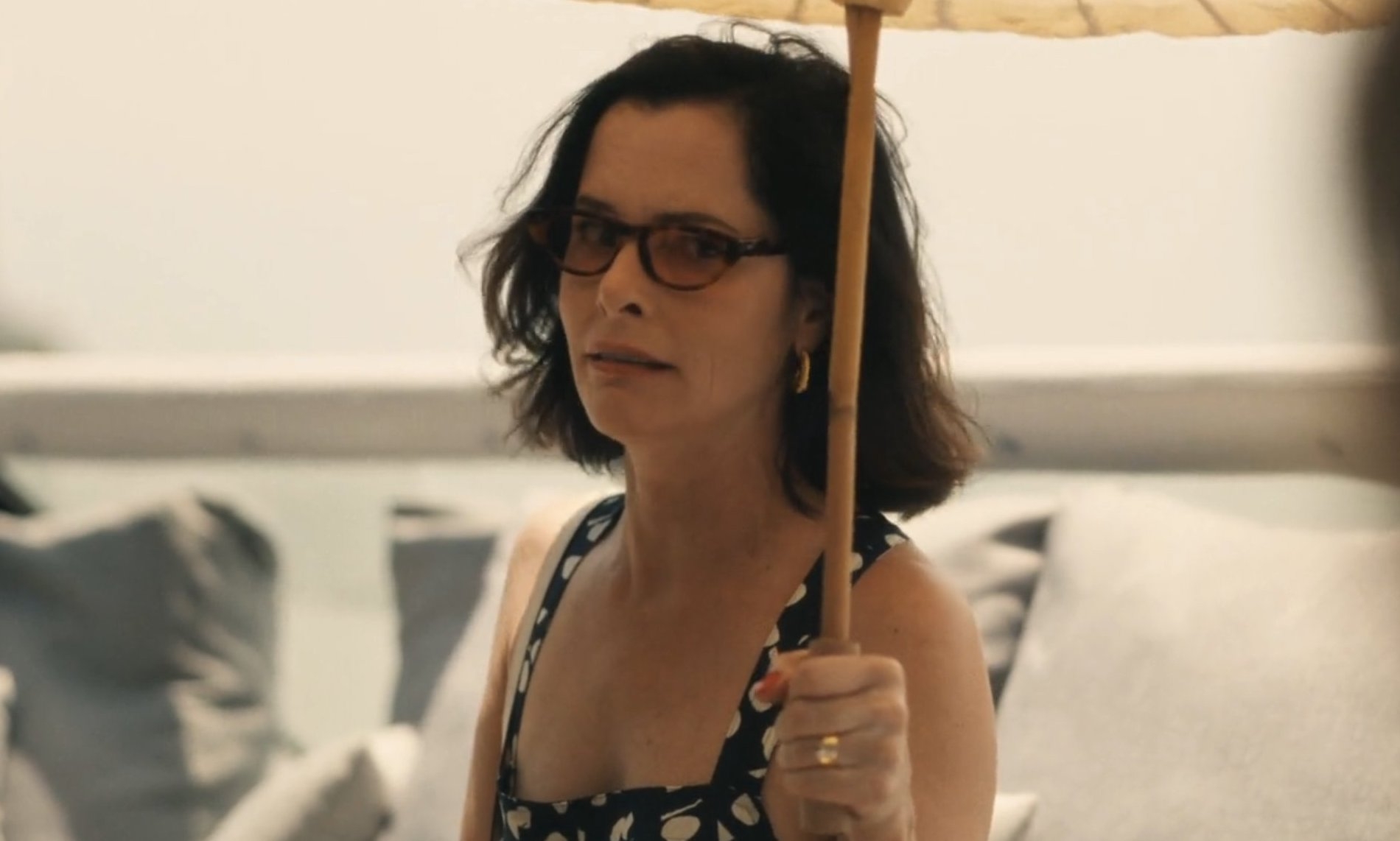 Woman in patterned sleeveless dress holding an umbrella outdoors, looking to the side