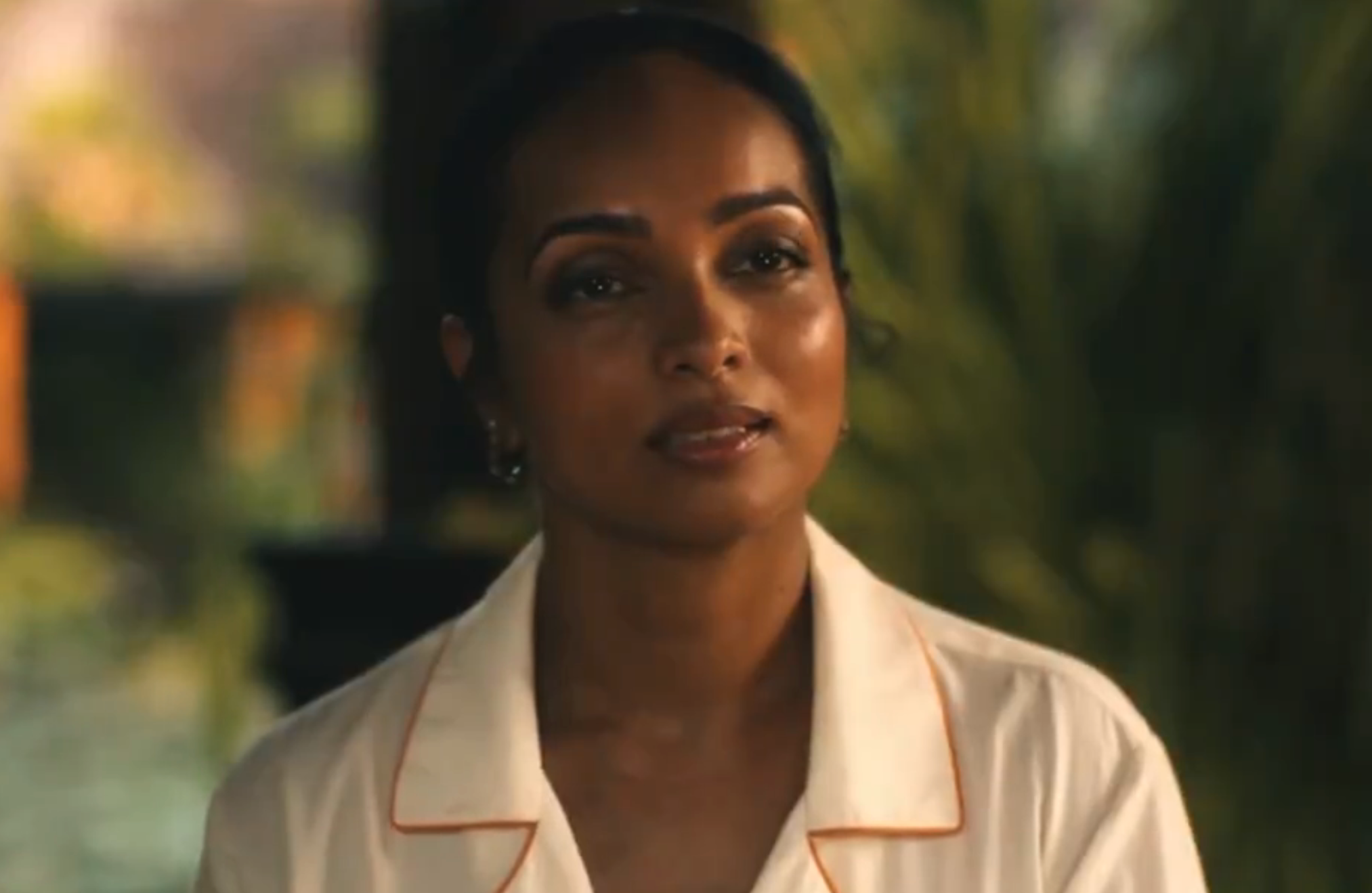 Person in a room, wearing a collared shirt, looks engaged in conversation. Background is blurred and indistinct