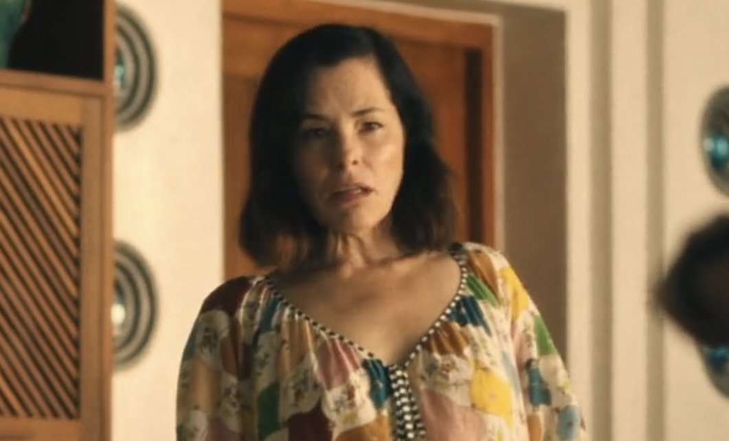 Person in a relaxed, patterned blouse stands indoors with a neutral expression