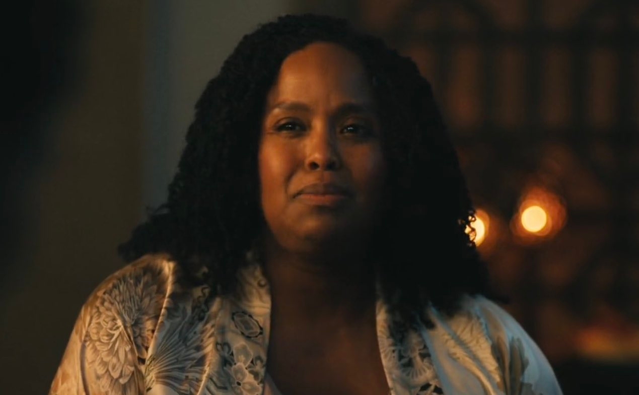 Person smiling softly, wearing a patterned robe, in a warmly lit setting with candles blurred in the background