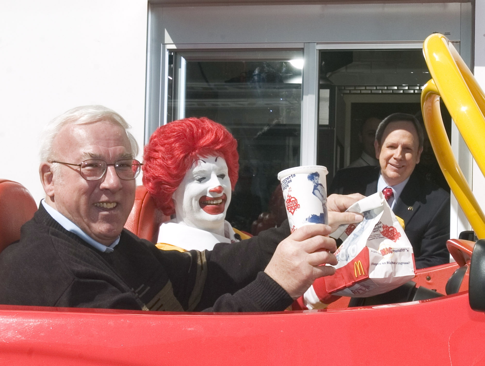 People in a car at a drive-thru, with one dressed as a clown, getting food from a McDonald’s window