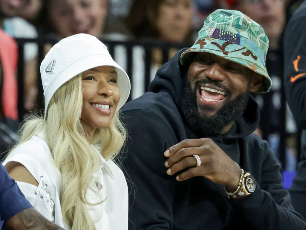 Two people smiling and sitting together, both wearing bucket hats, enjoying a public event