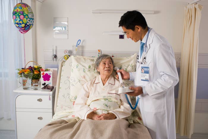 Doctor in a white coat checks on a smiling patient in a hospital bed, with a "Get Well Soon" balloon visible in the background