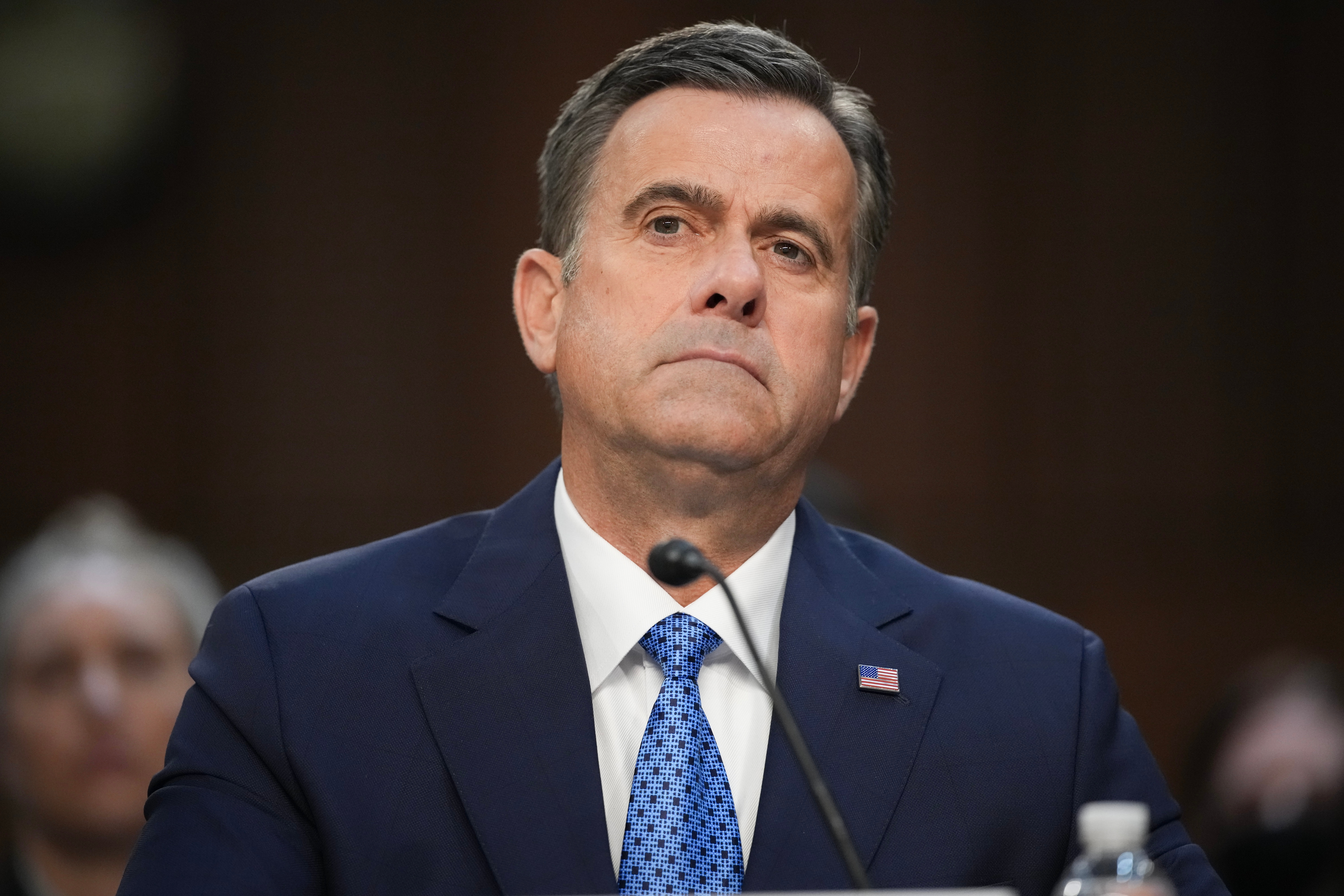 A person in a suit and tie attends an official event, appearing serious and attentive